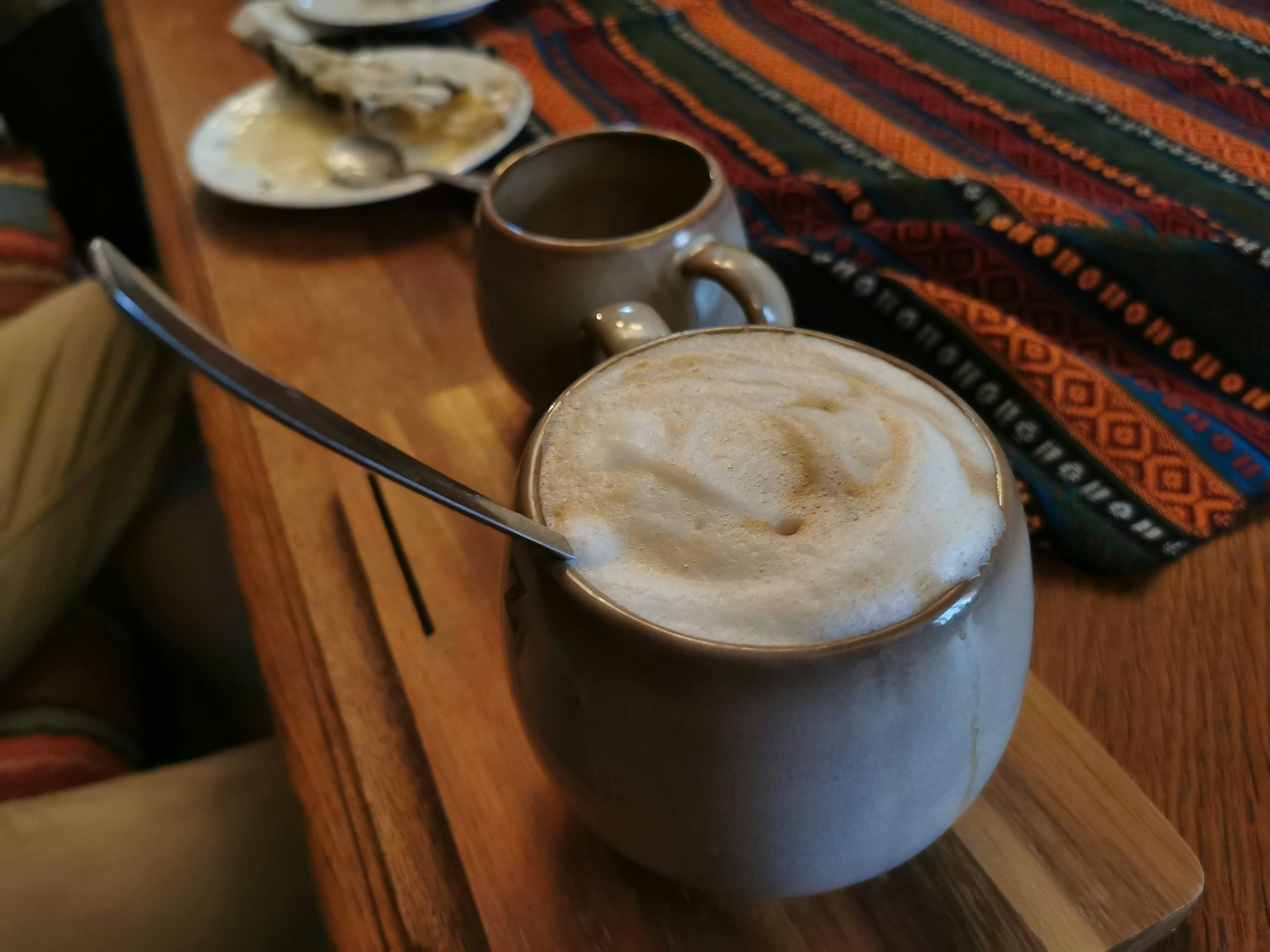 Un cappuccino mousseux dans une tasse en céramique avec une cuillère posée sur un plateau en bois