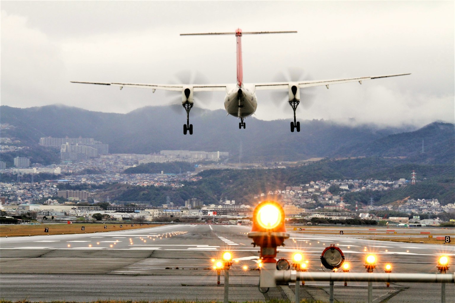 Image d'un avion atterrissant à un aéroport avec des montagnes et une ville en arrière-plan