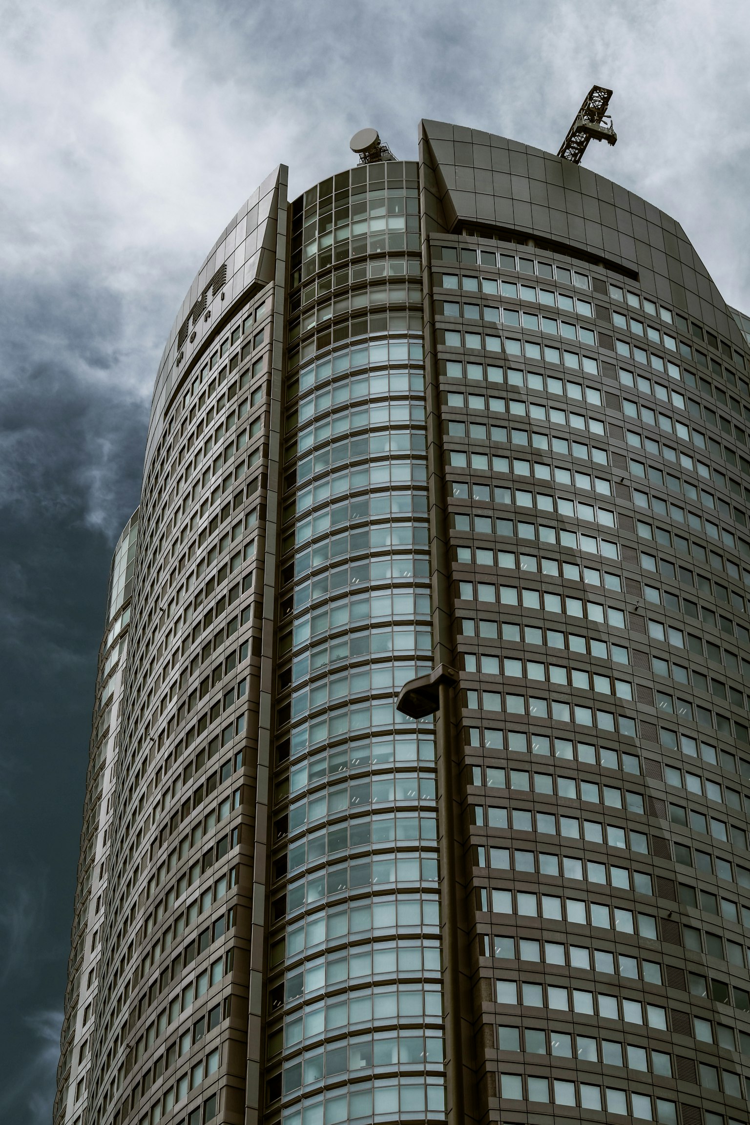 Cận cảnh tòa nhà chọc trời với cửa sổ phản chiếu dưới bầu trời nhiều mây có cần cẩu xây dựng