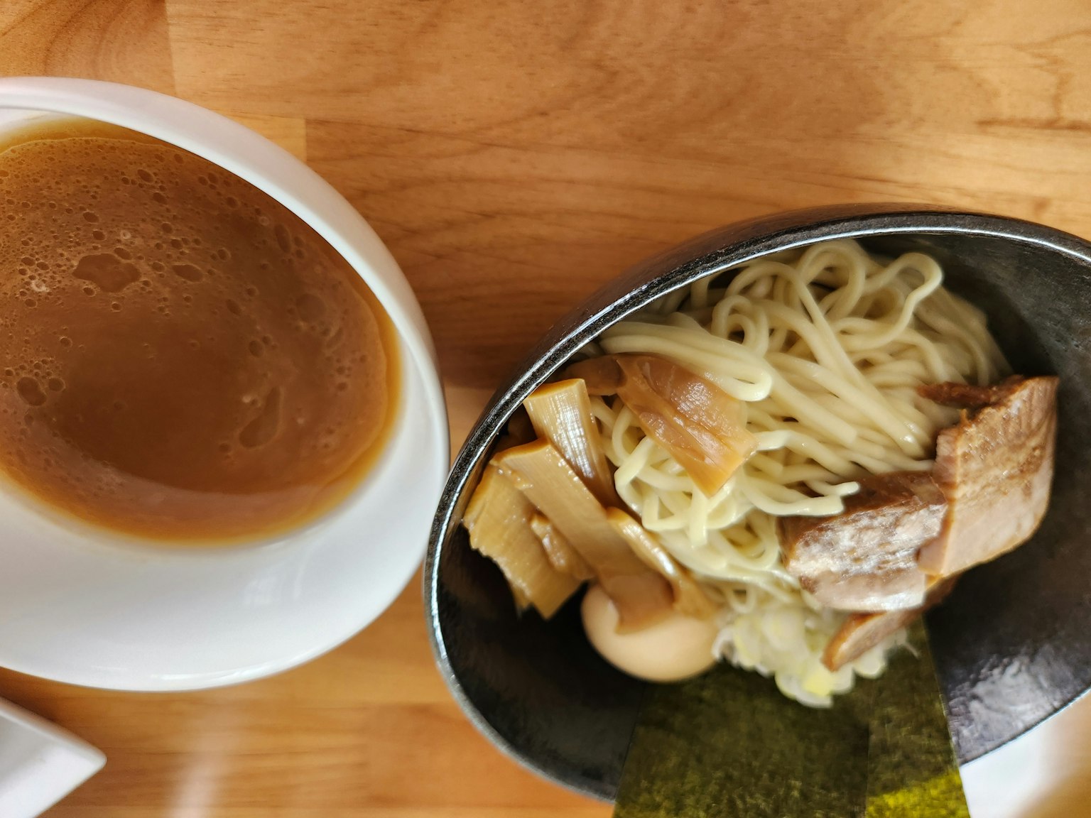 Bol de nouilles avec des garnitures incluant de la viande et des algues à côté d'une tasse de bouillon