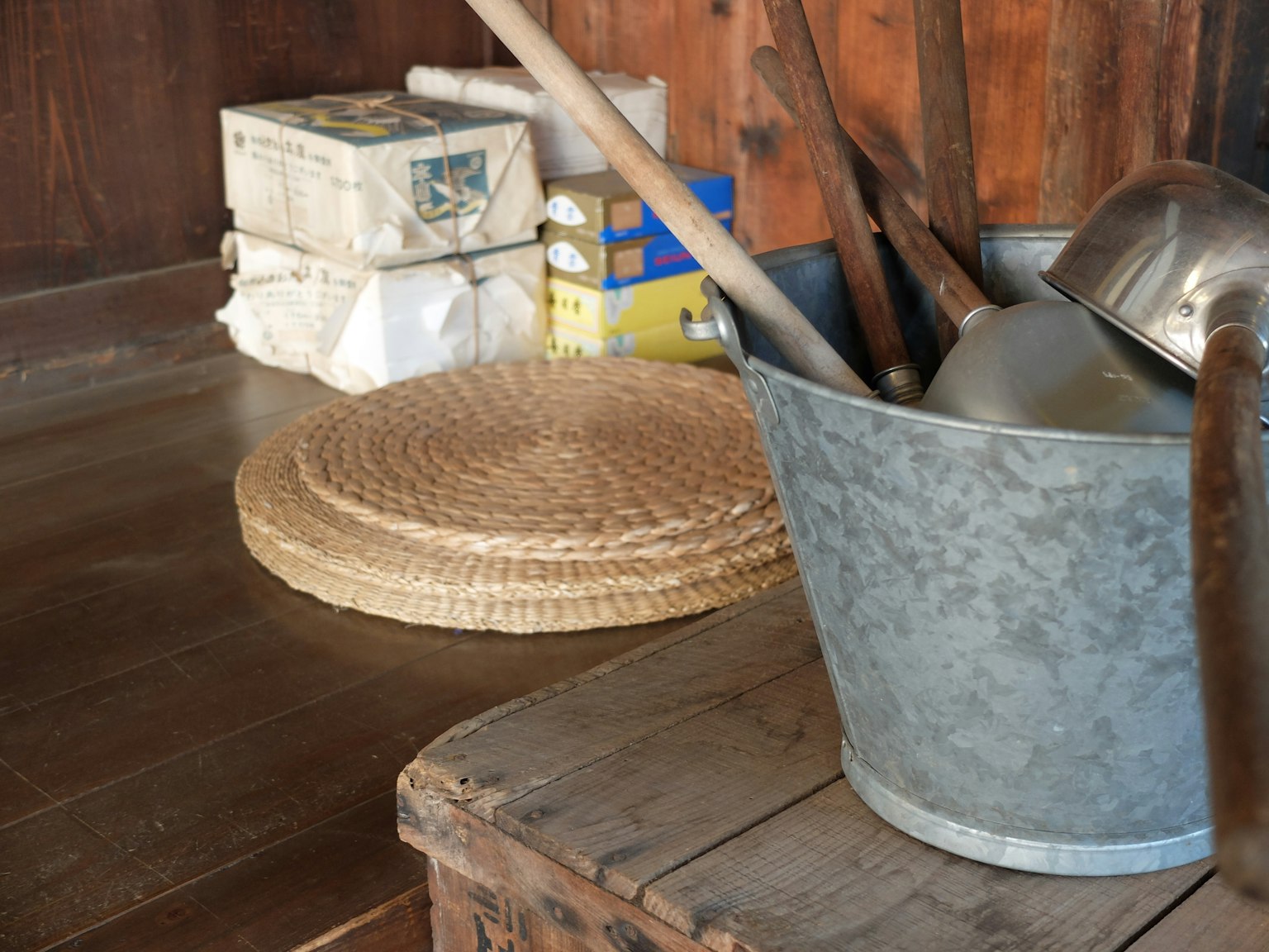 A simple corner of a room featuring a metal bucket and a straw mat on the wooden floor