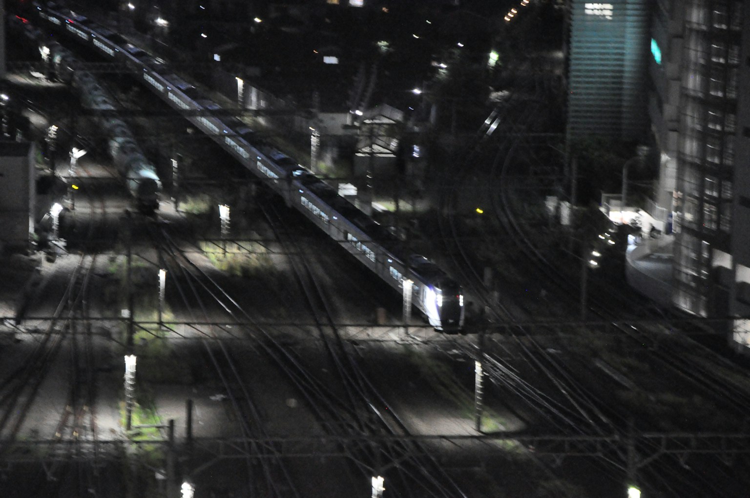 Scena notturna di una stazione ferroviaria con binari e luci dei treni