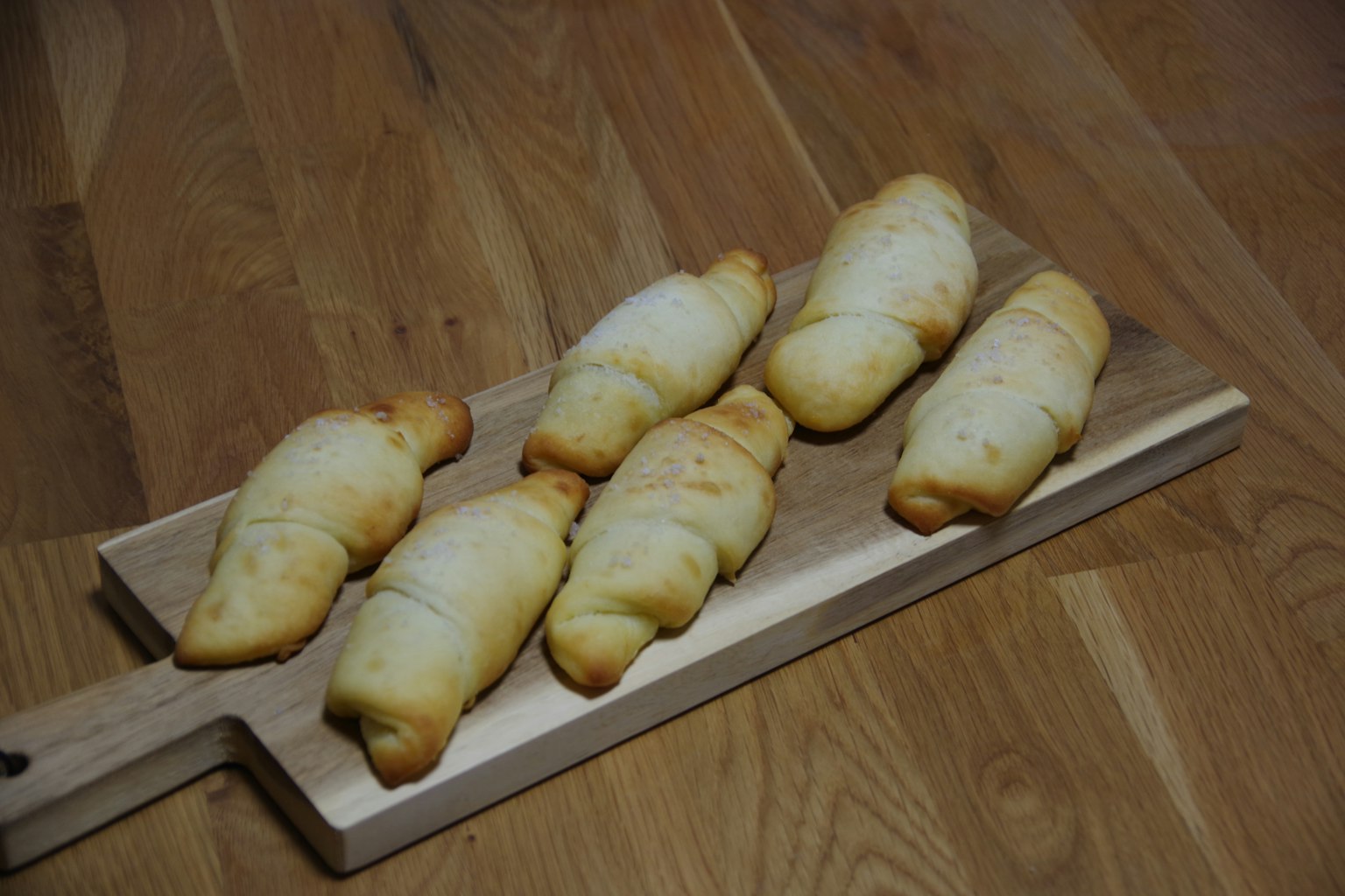 Sechs frisch gebackene Croissants auf einem Holzbrett angeordnet