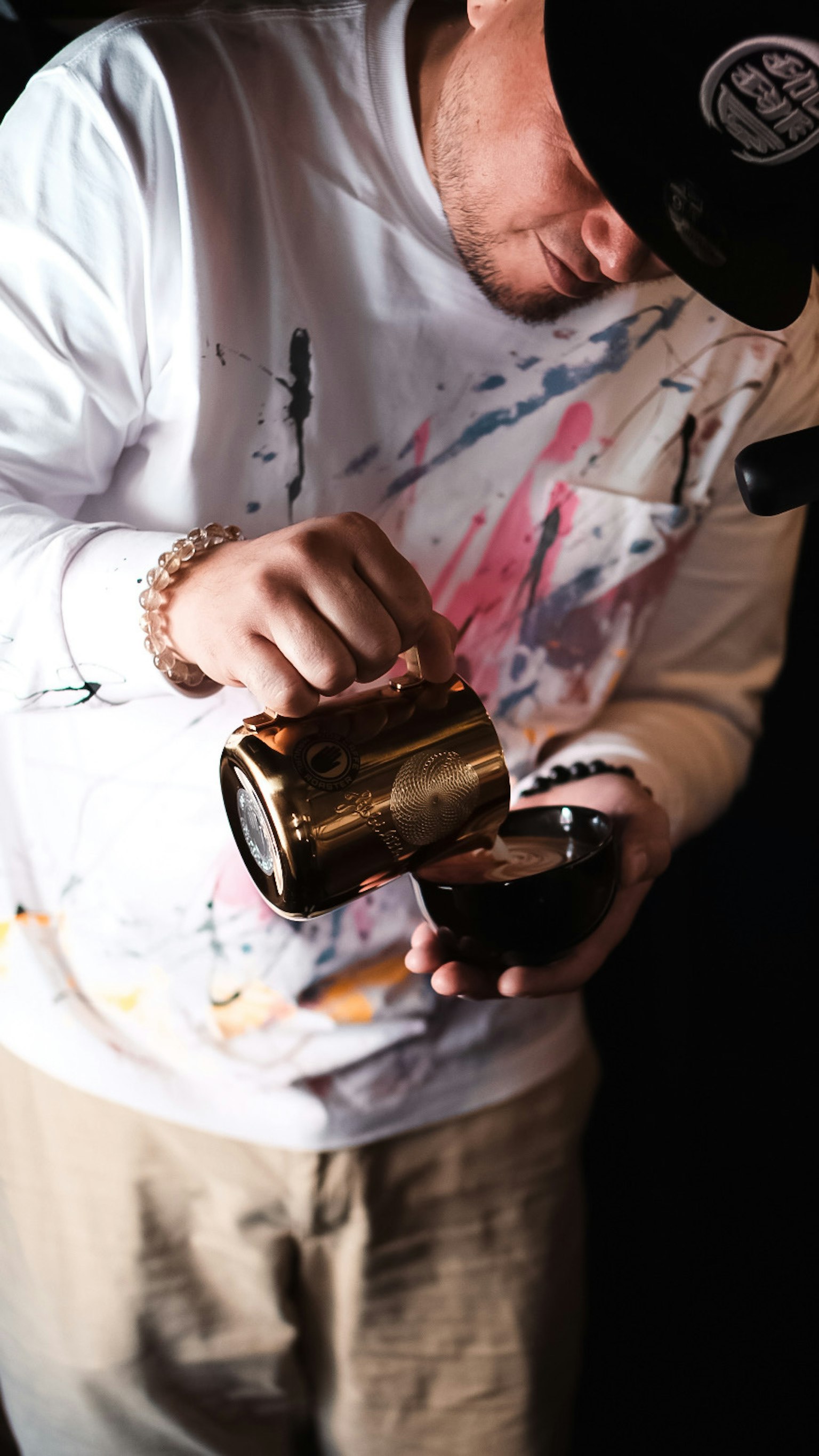 Ein Mann, der aus einer goldenen Tasse gießt, trägt ein farbenfrohes, bespritztes Shirt