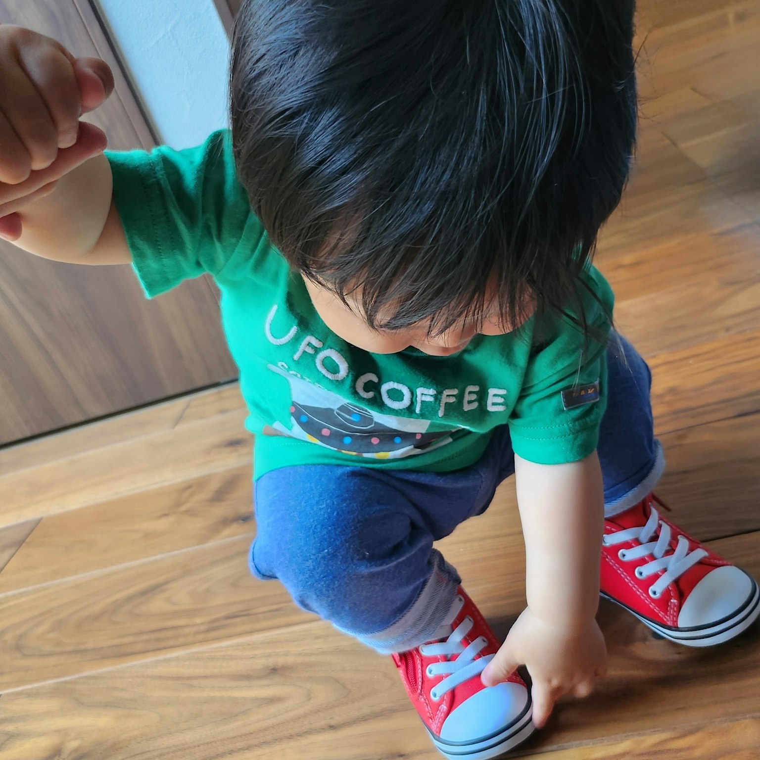 Trẻ nhỏ mang giày đỏ đang ngồi xổm trên sàn gỗ