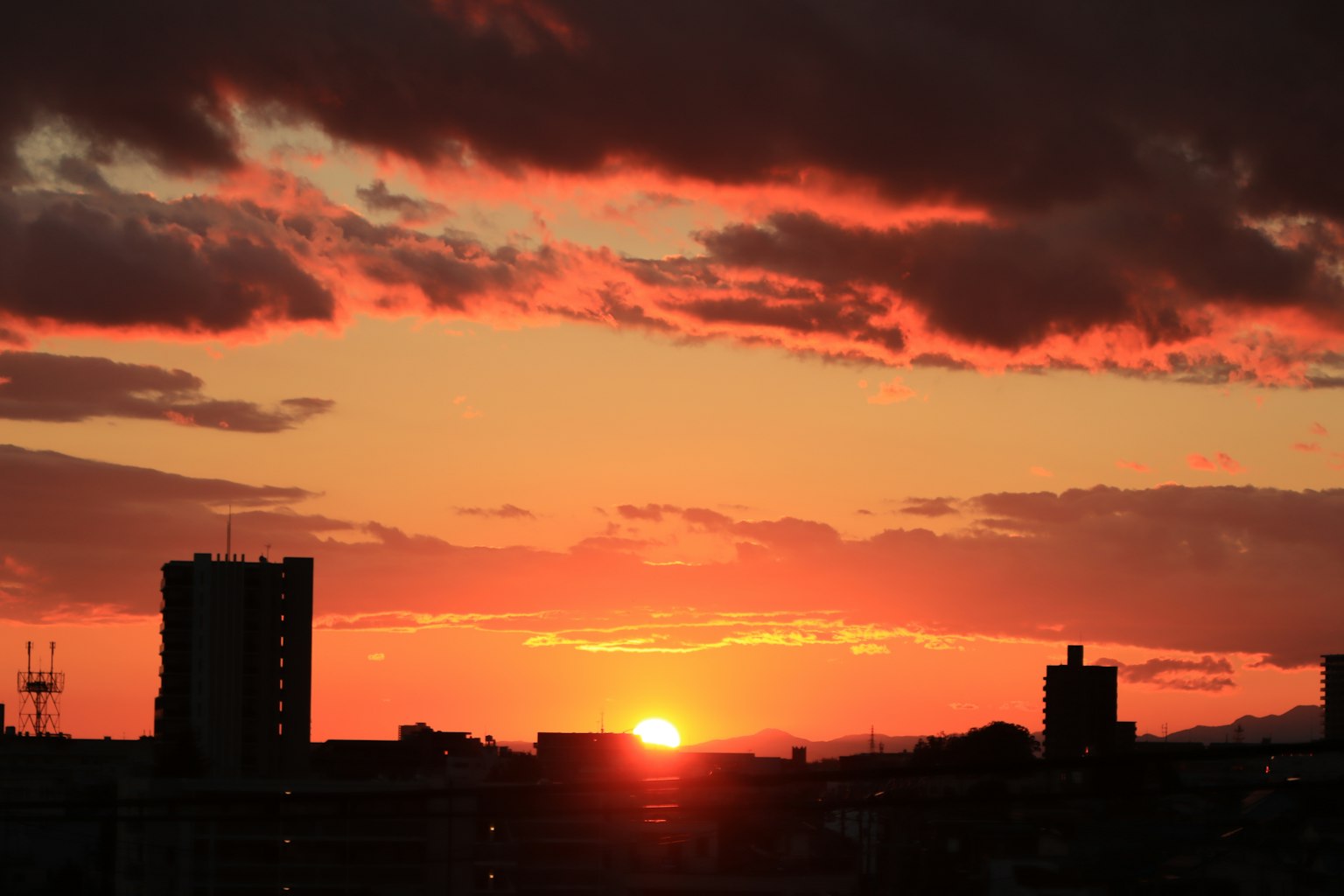 Stadtansicht bei Sonnenuntergang mit orangefarbenen Wolken und silhouettierten Gebäuden