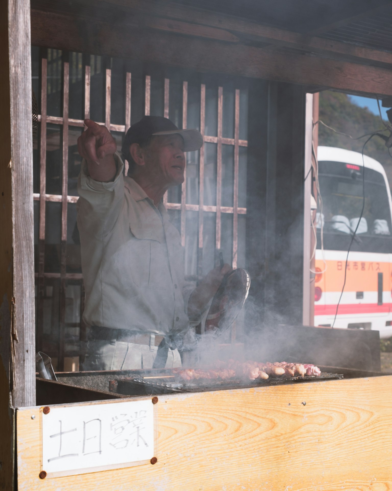 Pria memasak di warung makanan dikelilingi asap dan makanan panggang