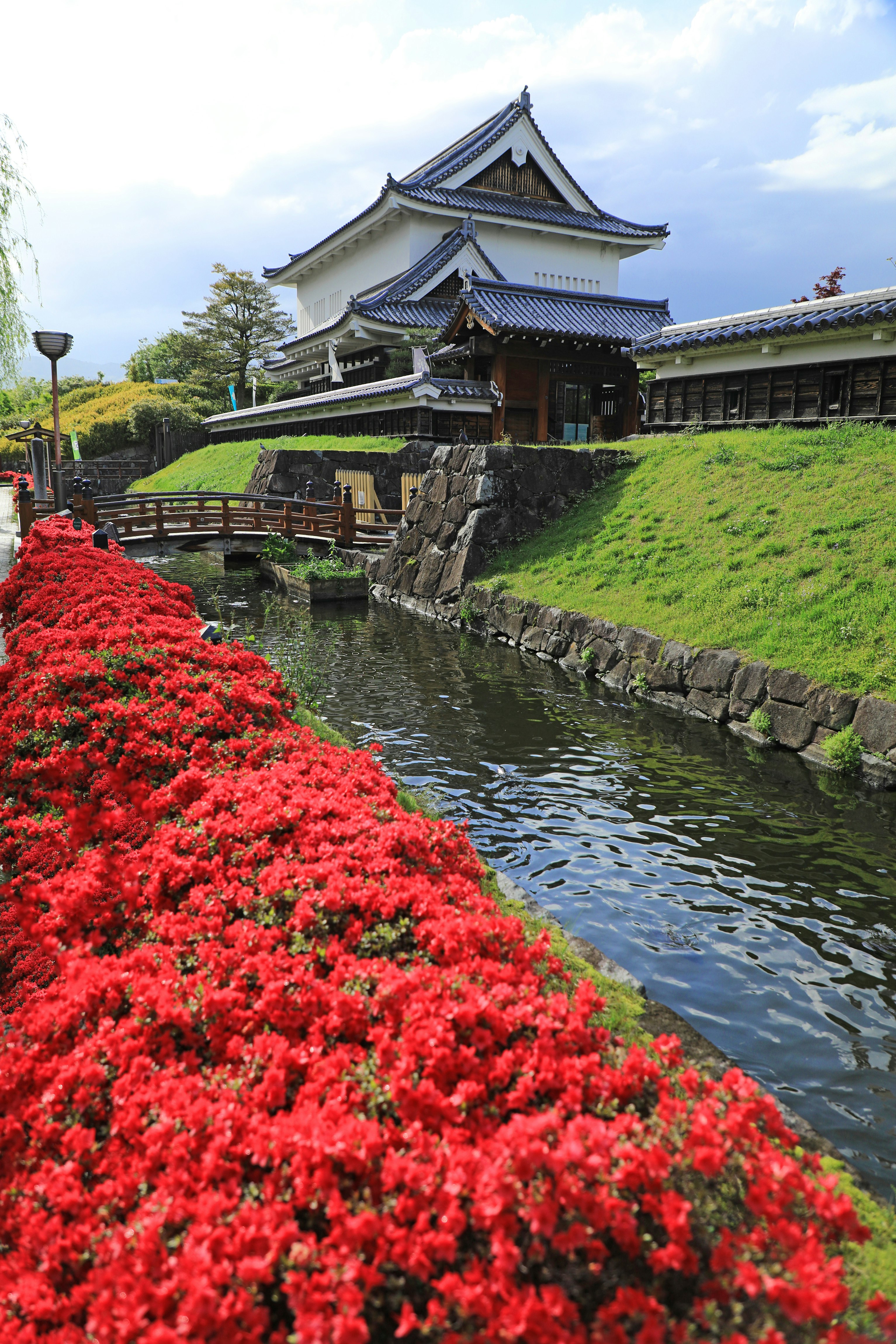 赤い花と水路沿いの寺院の石垣と屋根