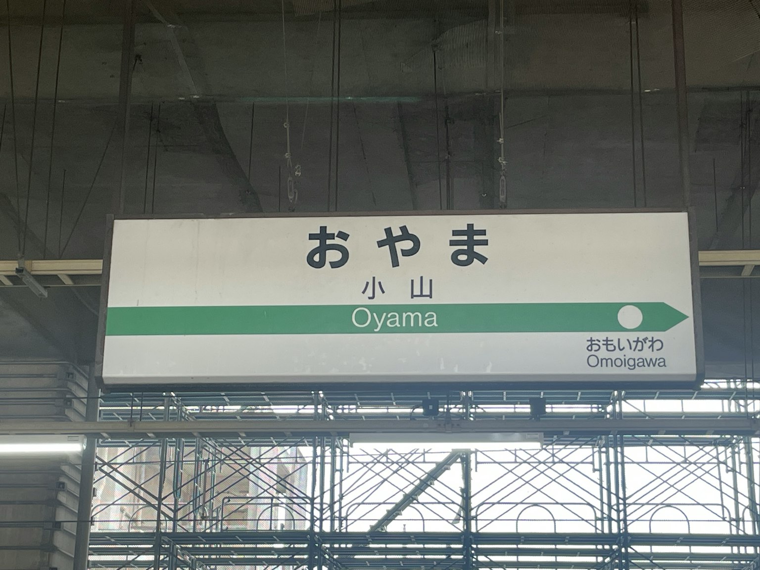 Papan tanda Stasiun Oyama dengan teks dalam bahasa Jepang dan Inggris