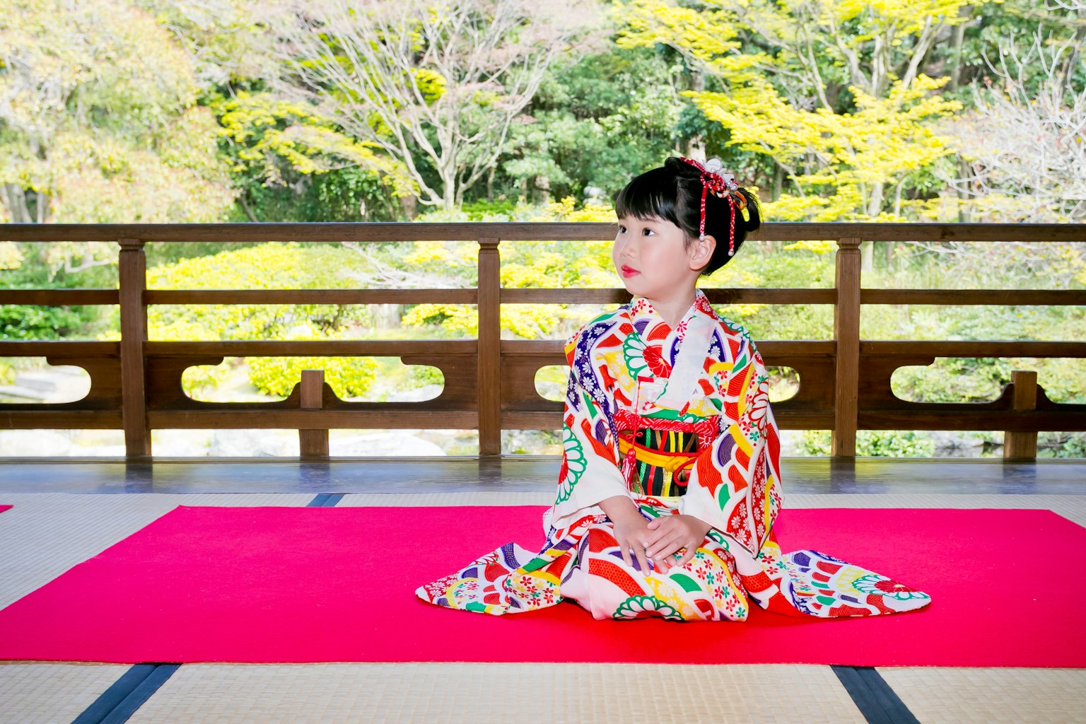 Cô gái trong bộ kimono xinh đẹp ngồi trên thảm đỏ với nền là cây cối xanh tươi