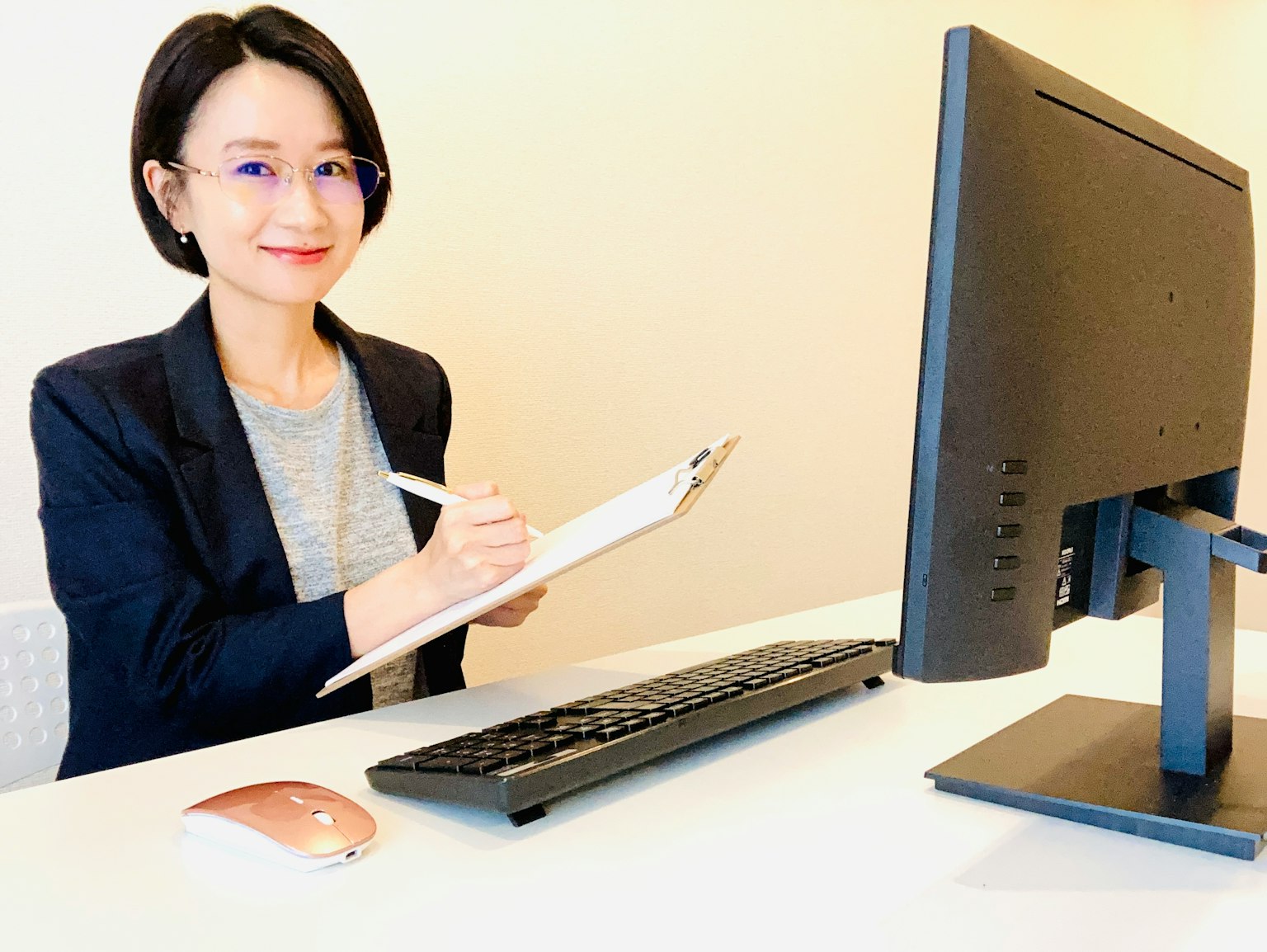 Una donna che lavora a una scrivania sorridendo mentre prende appunti su un clipboard
