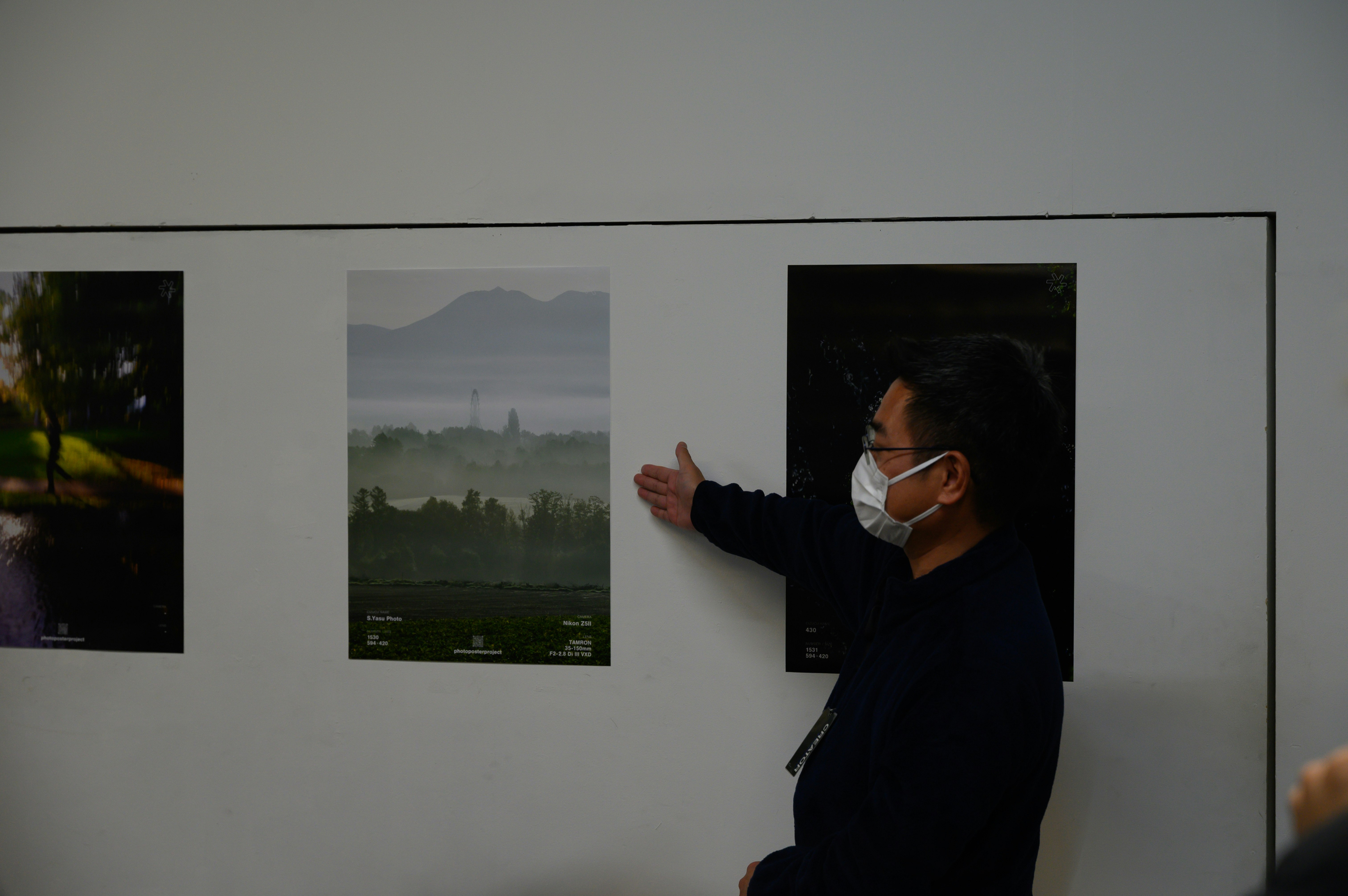 壁に掛けられた展示ポスターとマスク姿の人物