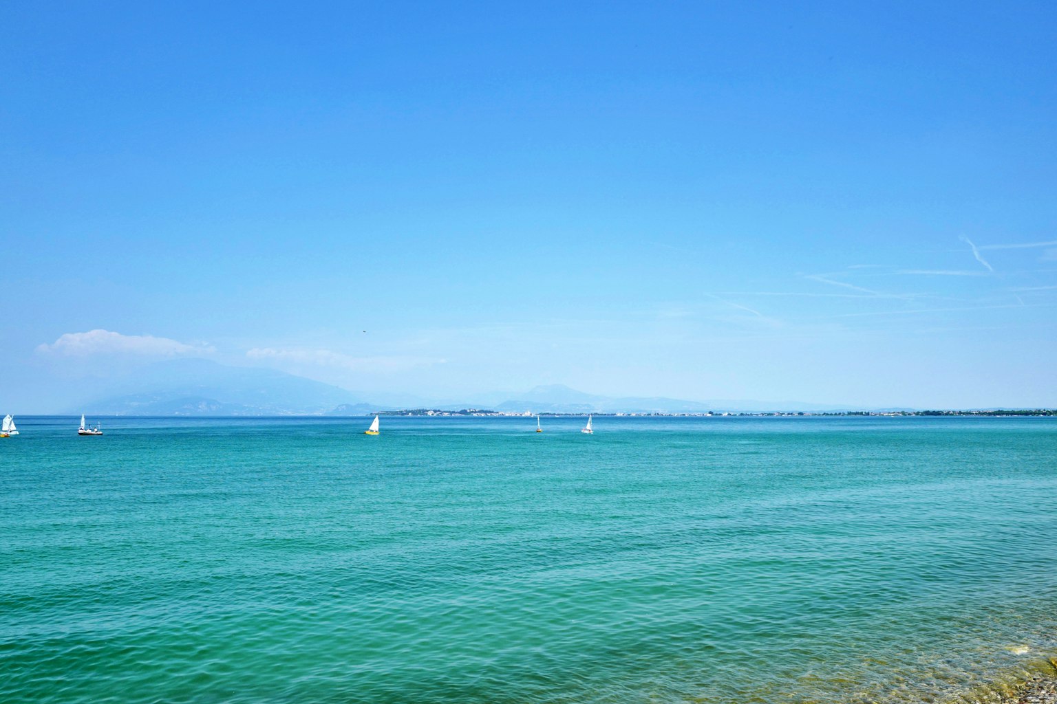 Klarer blauer Himmel mit ruhiger See und weißen Segelbooten in der Ferne