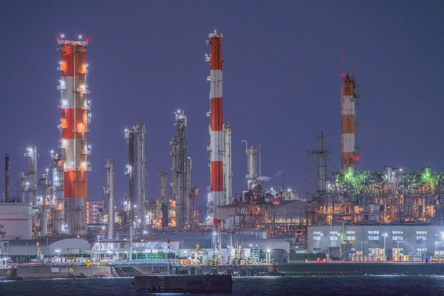 Industrieller Komplex bei Nacht mit beleuchteten Schornsteinen