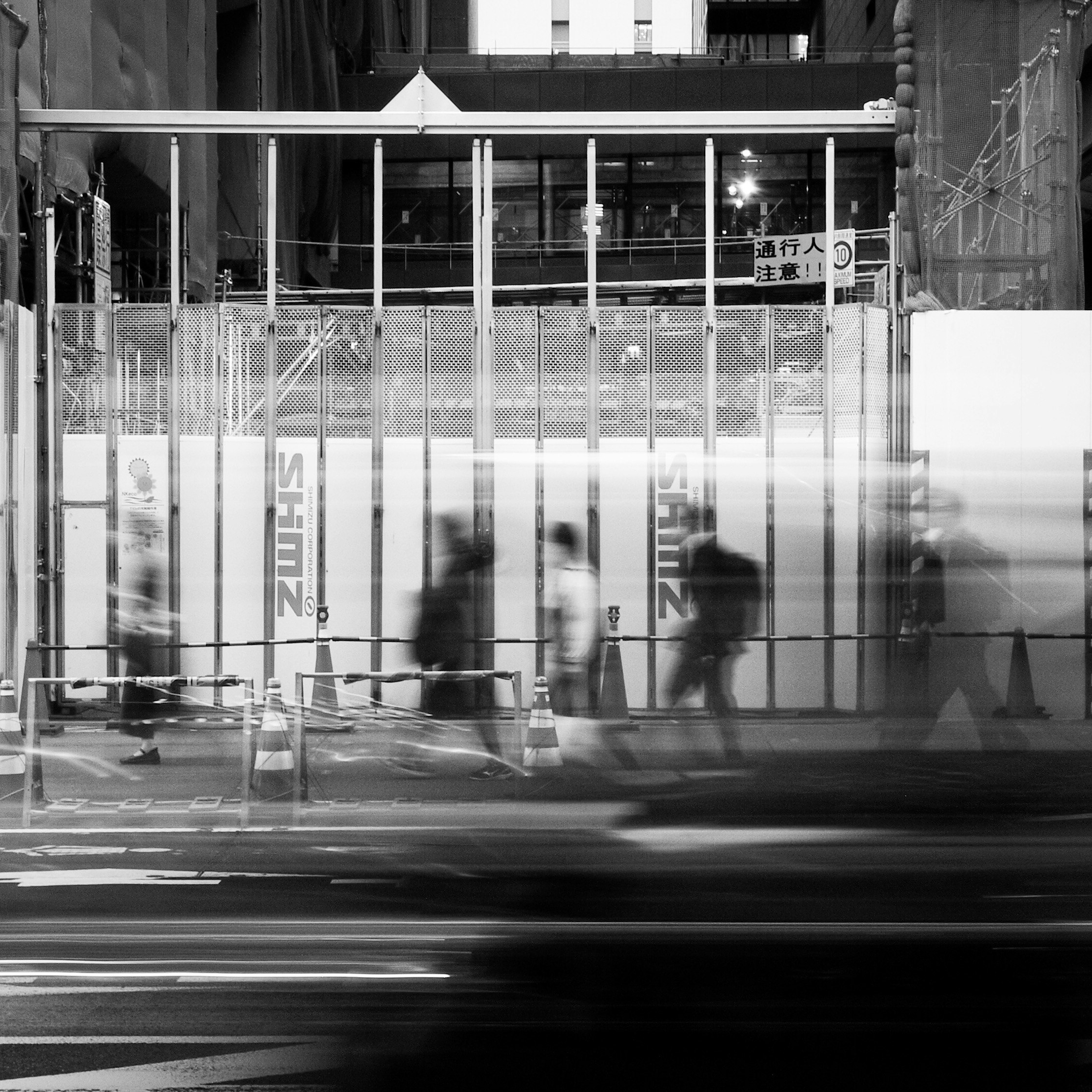 工事中の高架下で流れるタクシーと通行人のモノクロ風景