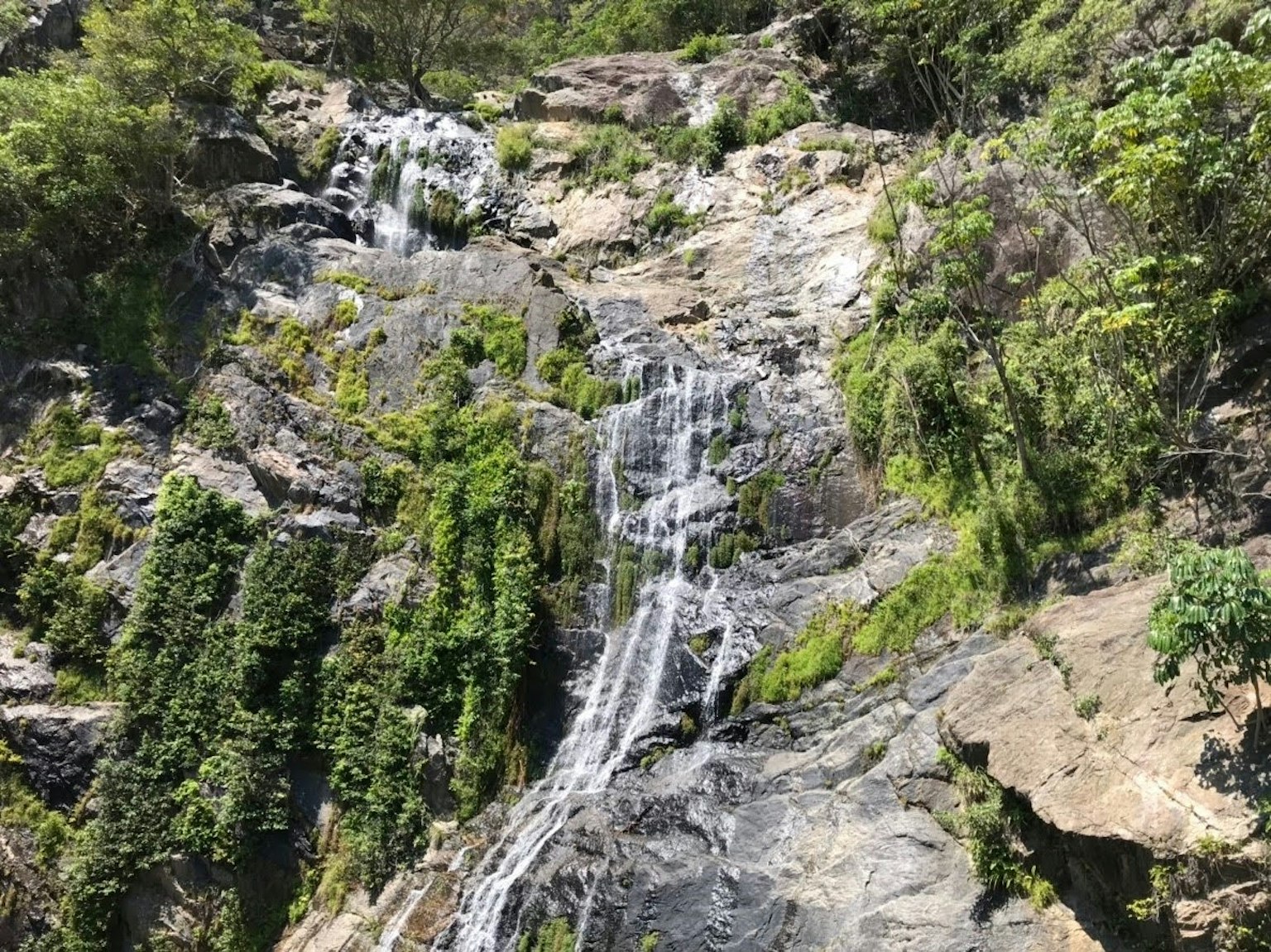 Air terjun indah mengalir di permukaan batu yang ditutupi vegetasi