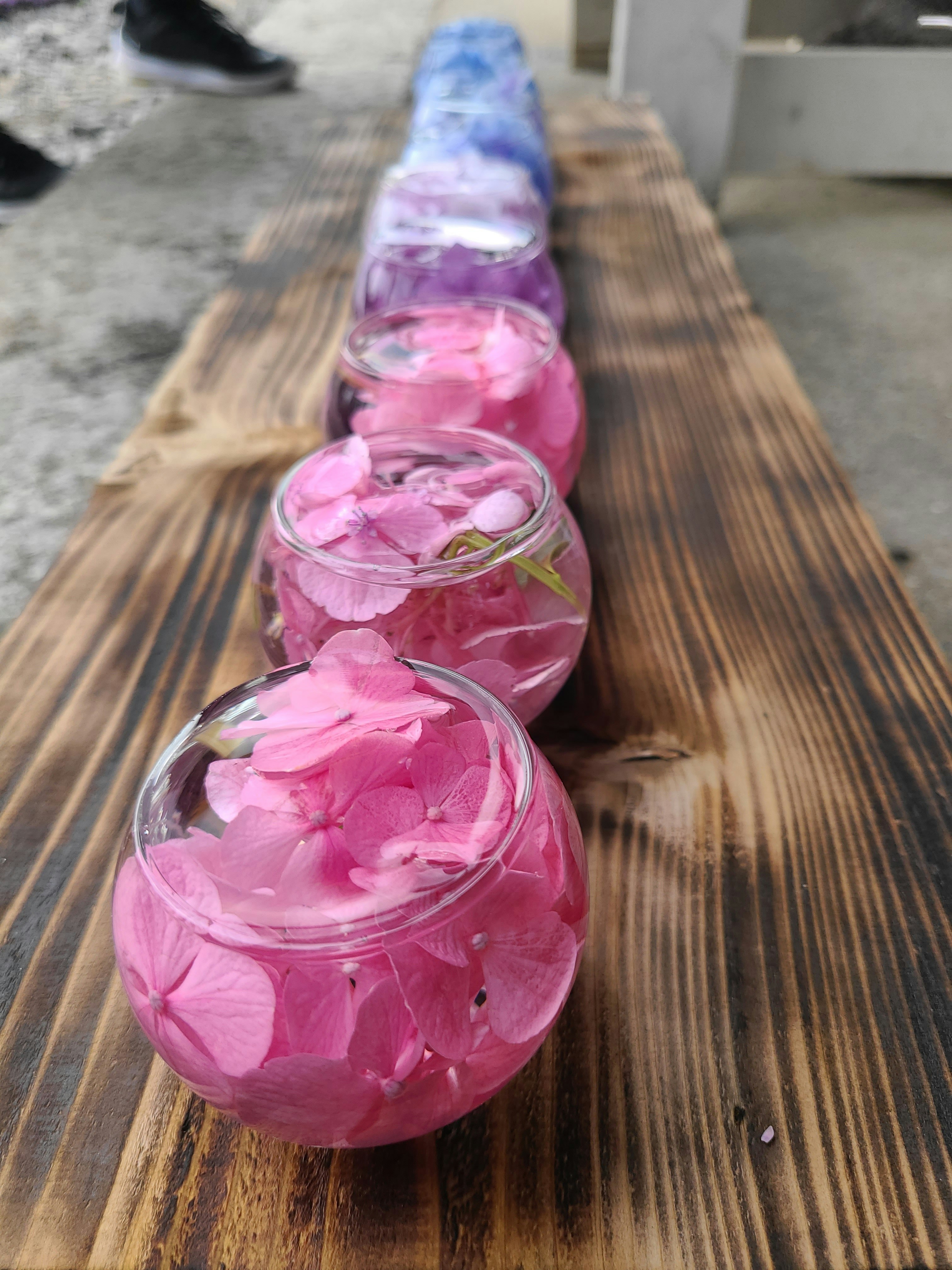 Auf einer Holzplatte aufgereihte Glasflaschen mit rosafarbenen Blütenblättern