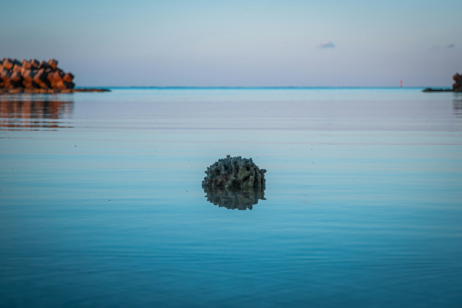 静かな水面に浮かぶ小さな岩のような物体と穏やかな青い空