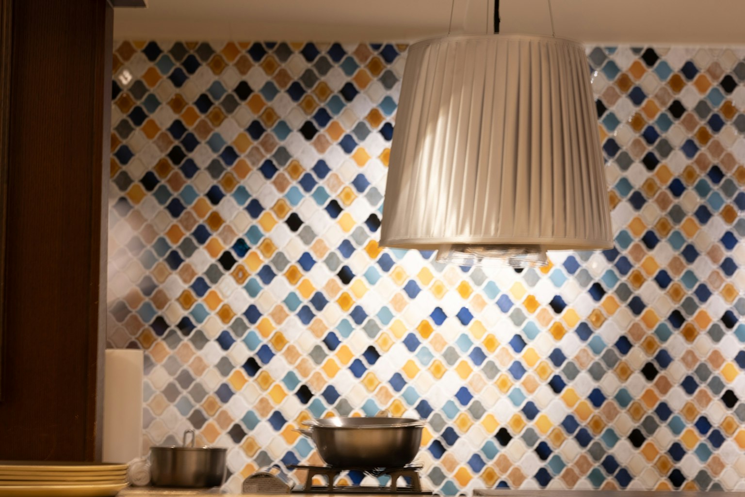 Interno di una cucina con un muro piastrellato colorato e una lampada a sospensione bianca