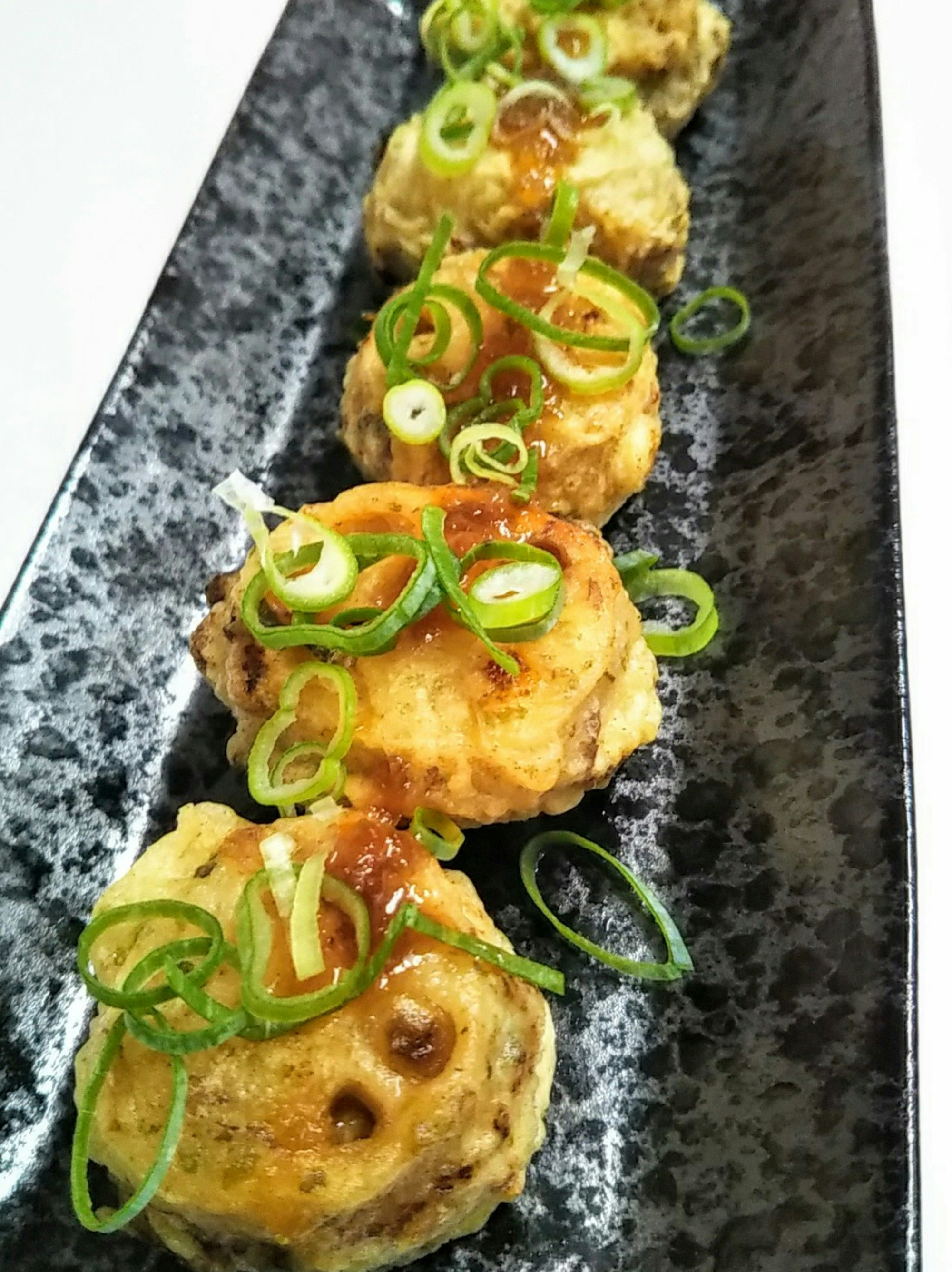 Japanische Lotuswurzel-Frittierstücke mit Frühlingszwiebeln garniert