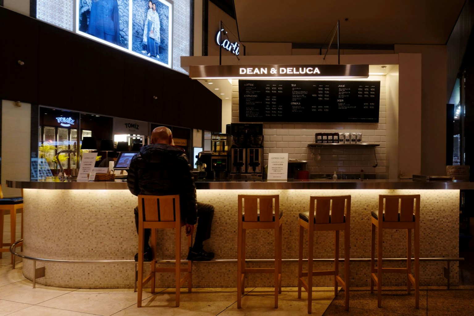 เคาน์เตอร์ร้านกาแฟพร้อมเก้าอี้ไม้และลูกค้านั่งอยู่