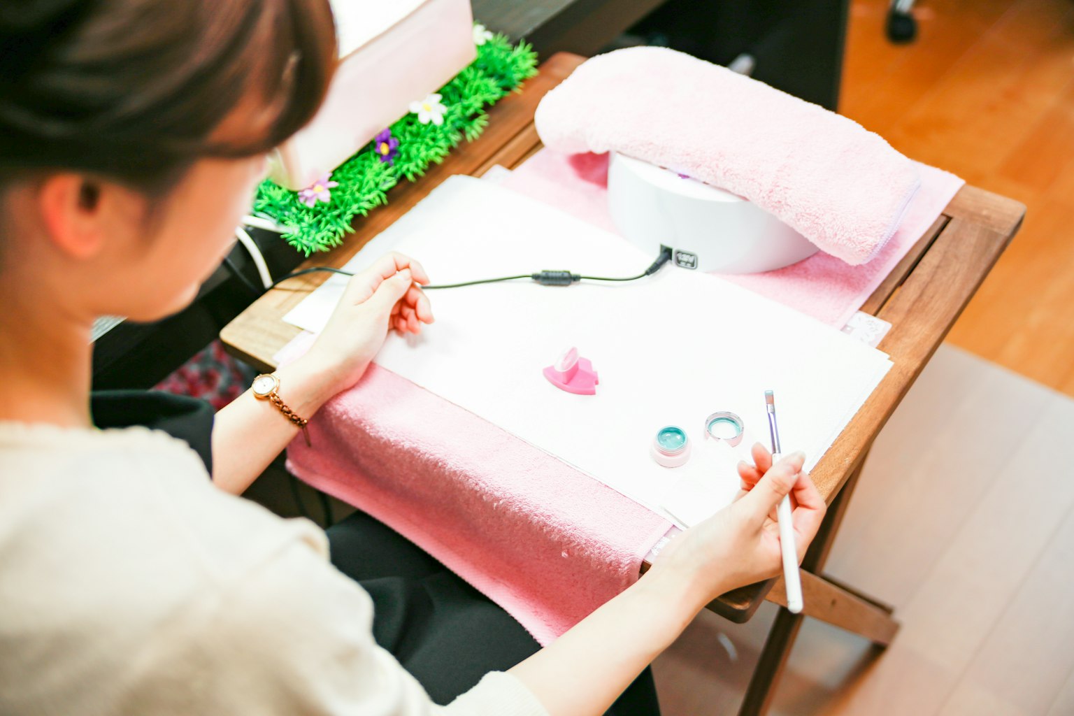Una mujer trabajando en arte de uñas con esmalte colorido sobre una toalla rosa