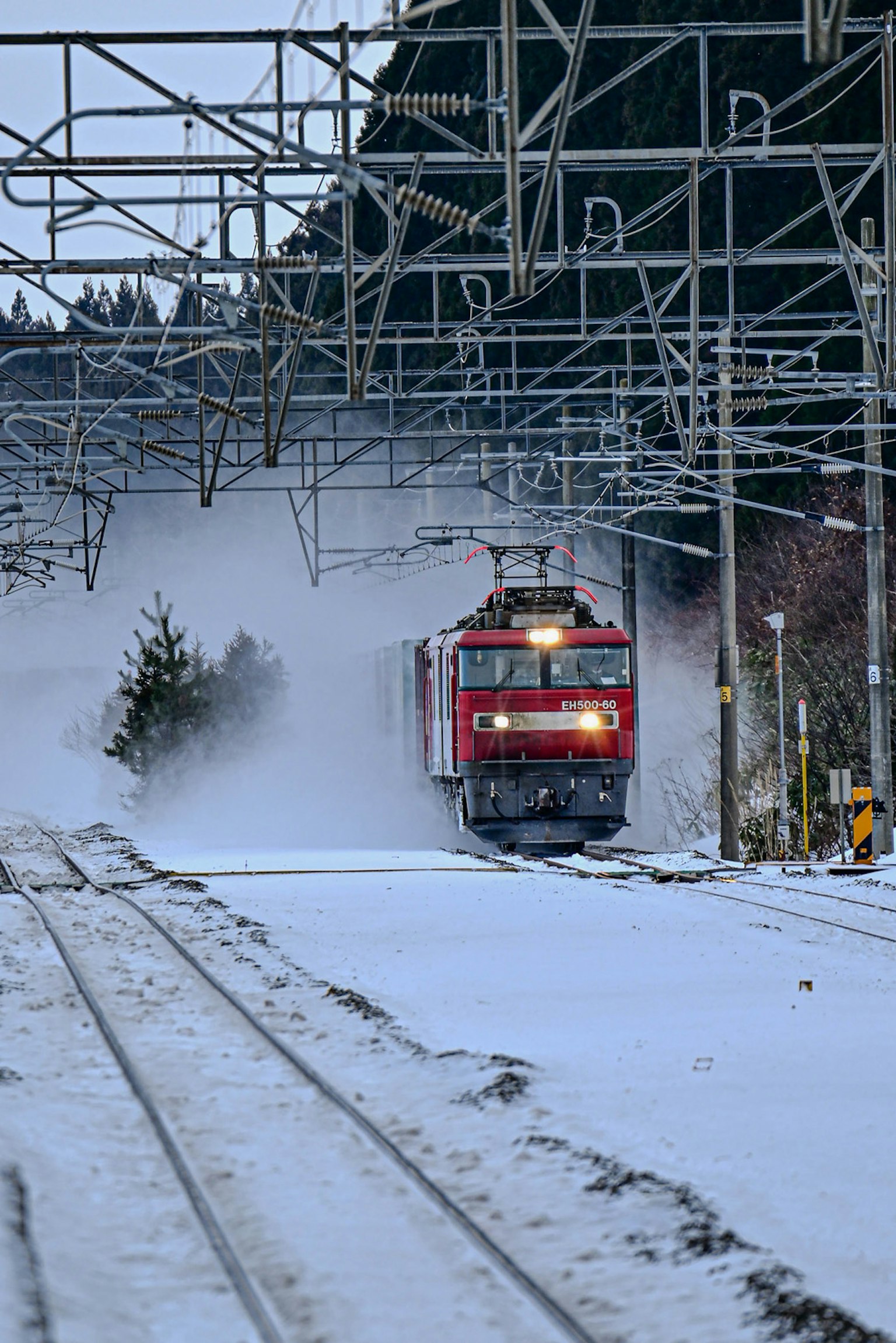 Red train moving through snow with surrounding power lines