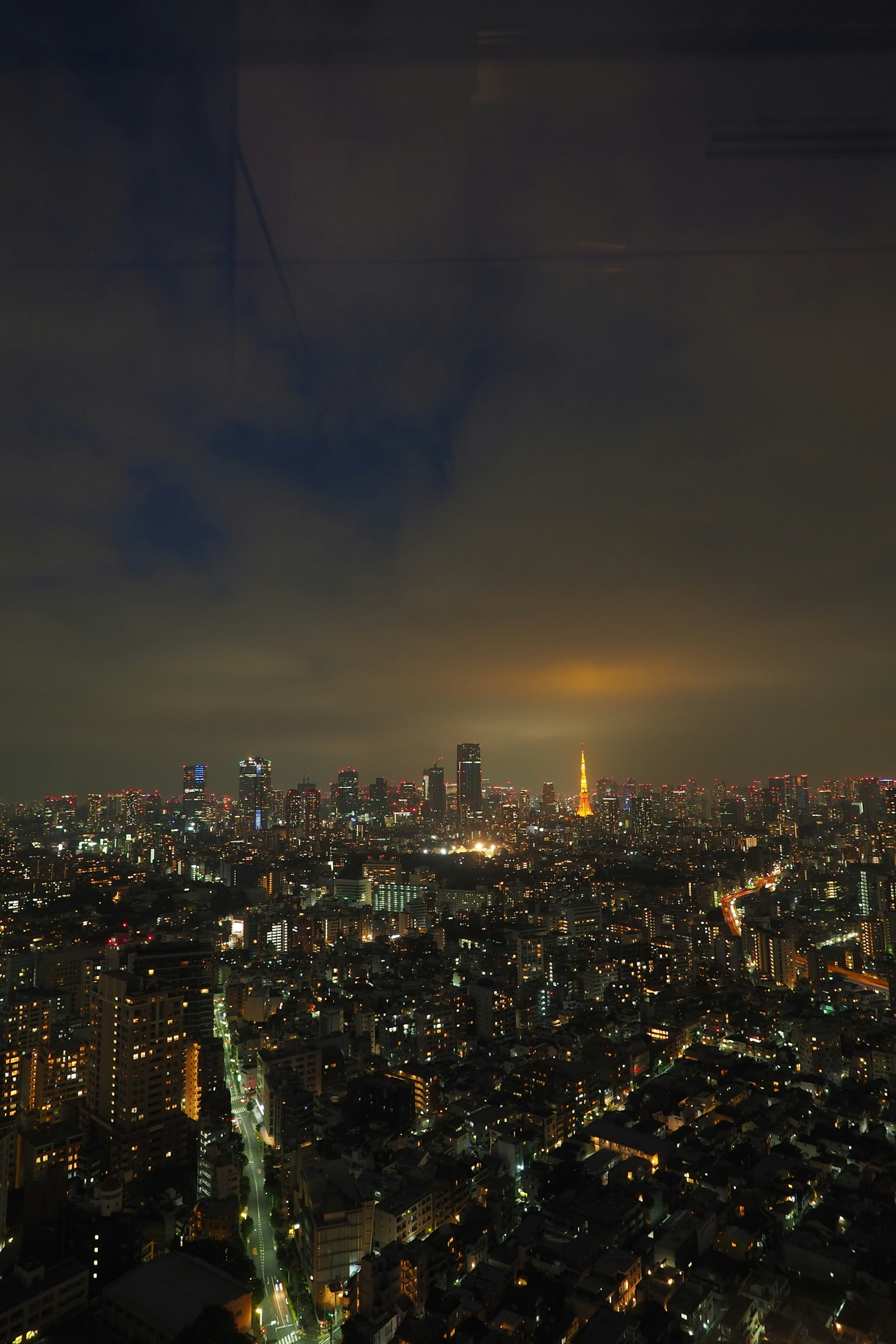 Khung cảnh thành phố Tokyo về đêm với các tòa nhà chọc trời và đèn đường sáng dưới bầu trời nhiều mây