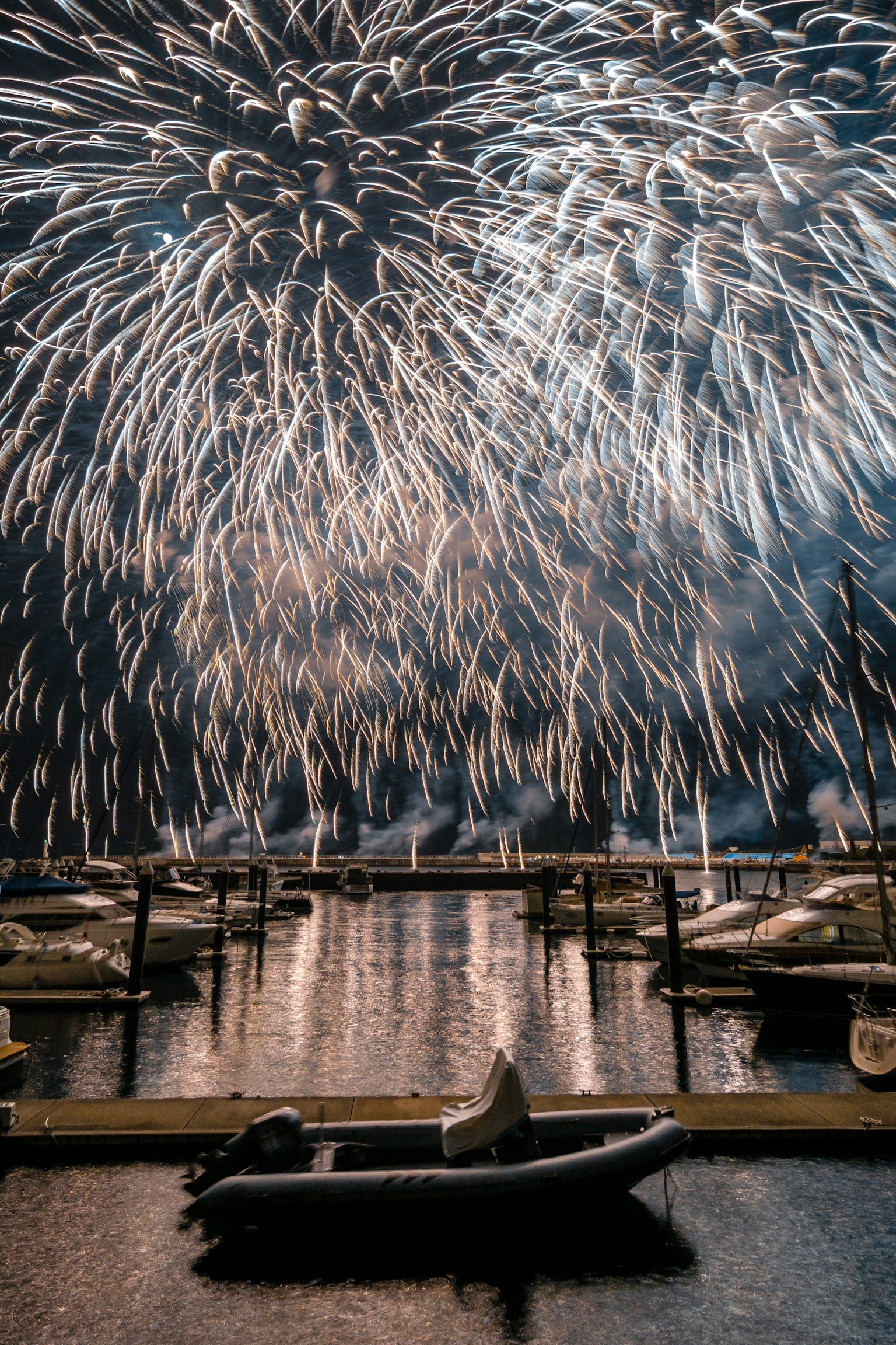 Feuerwerk, das im Nachthimmel über einem ruhigen Hafen mit Booten explodiert