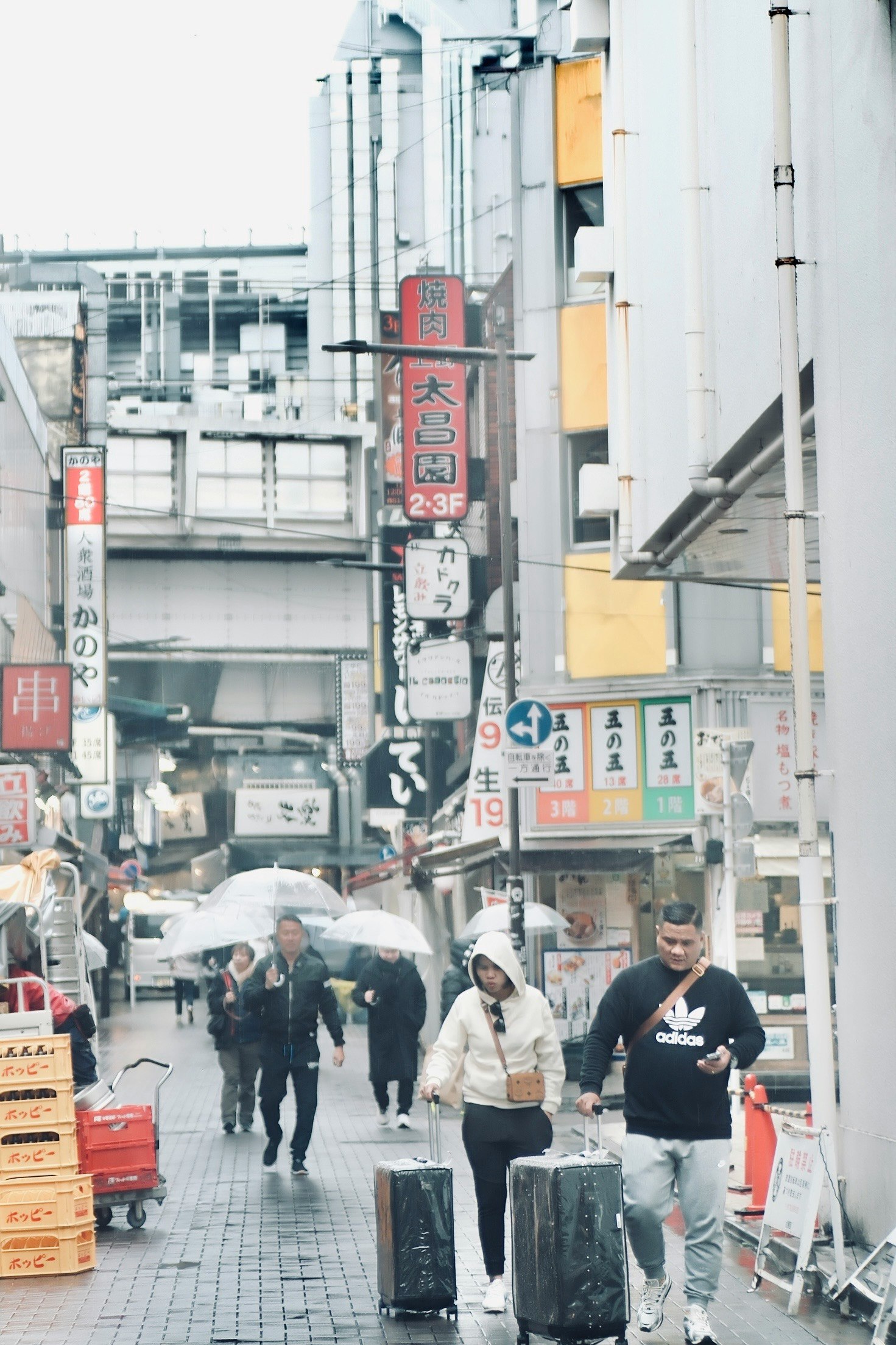 雨の商店街で傘をさす人々と看板の並ぶ通り
