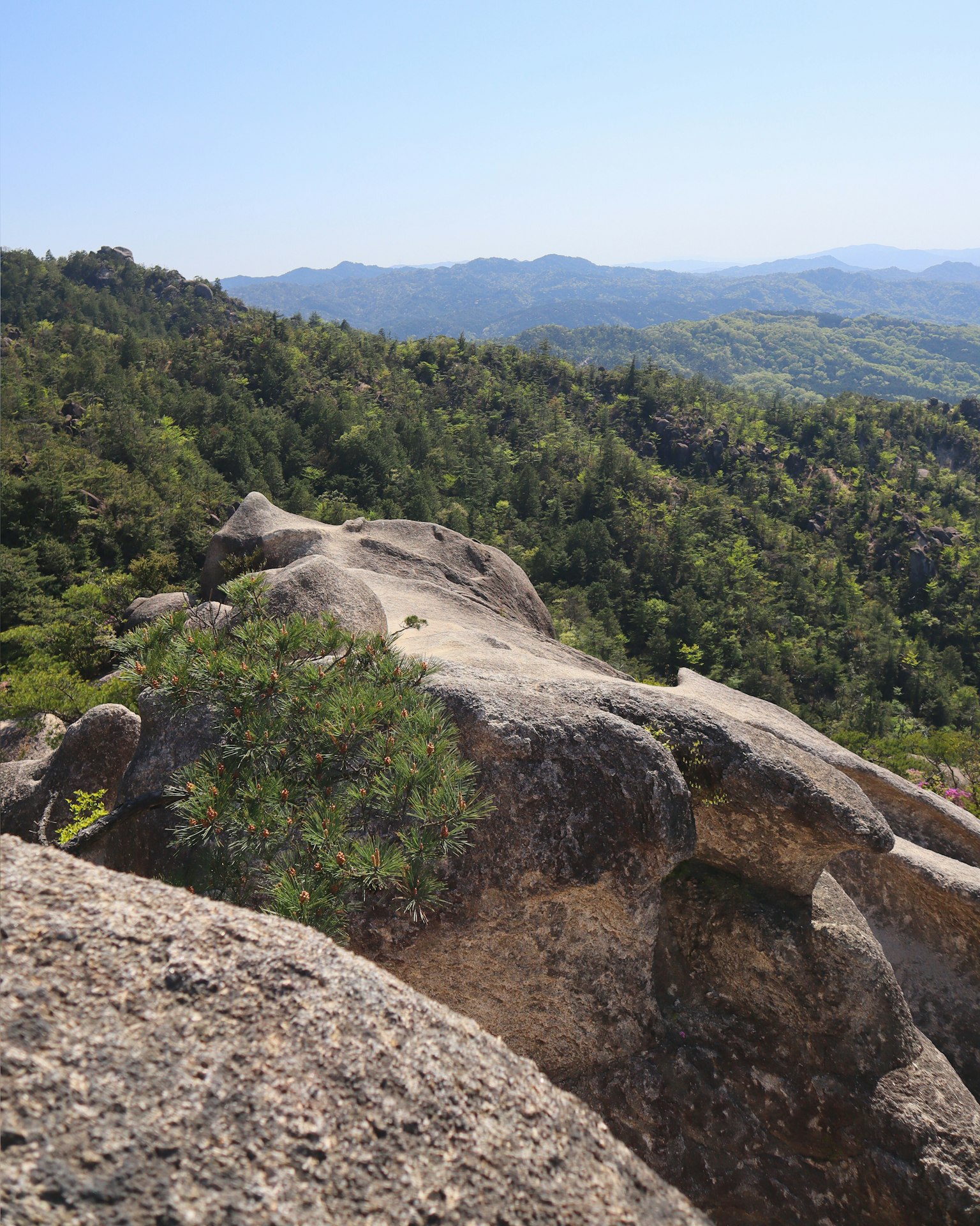 A scenic view from a rocky outcrop overlooking lush green hills and a blue sky