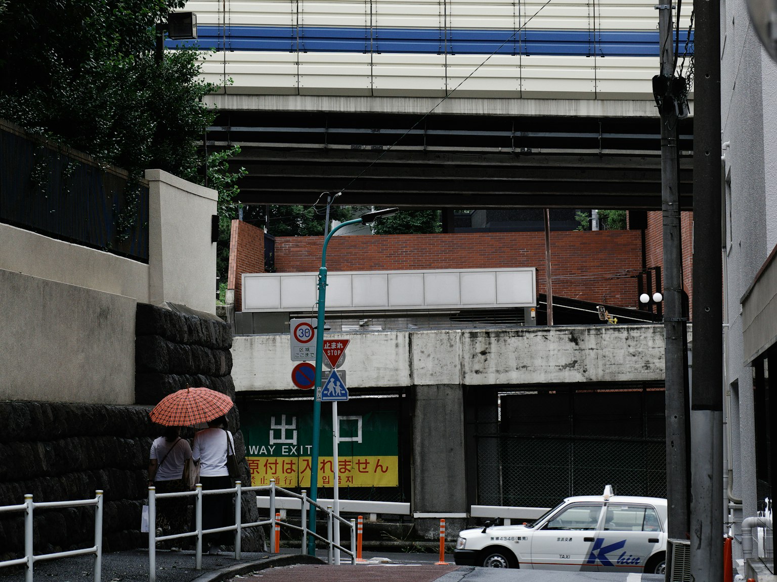 Street scene with a taxi and people under an umbrella near an overpass
