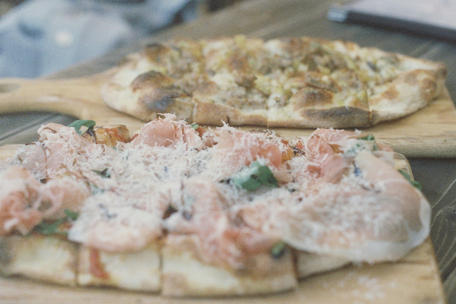 Two types of pizza with fresh toppings on wooden boards