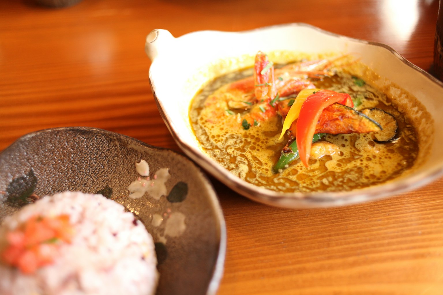 Un piatto di curry con verdure colorate e una ciotola di riso rosso accanto