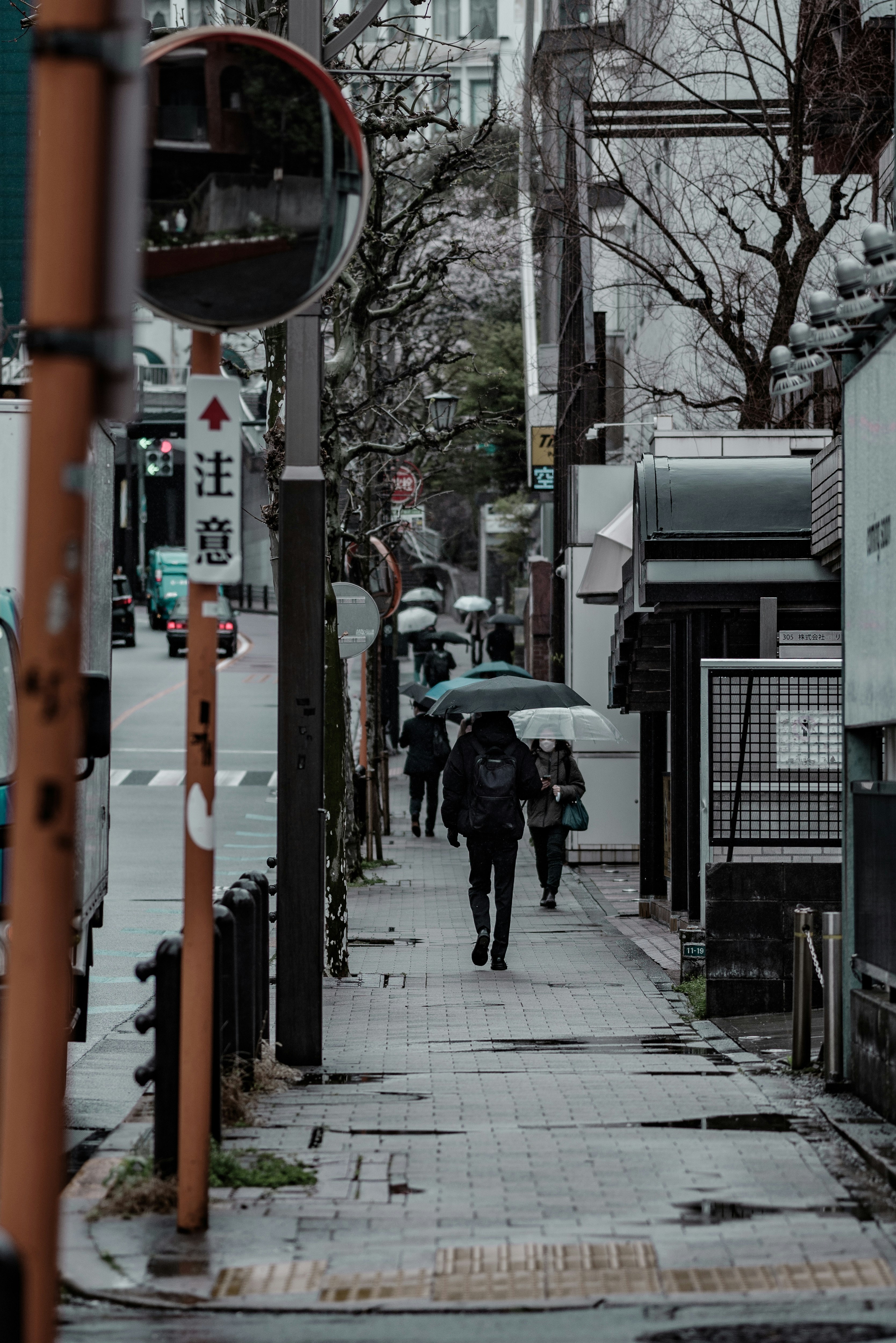 雨の降る乃木坂へ続く路地で傘をさす人々