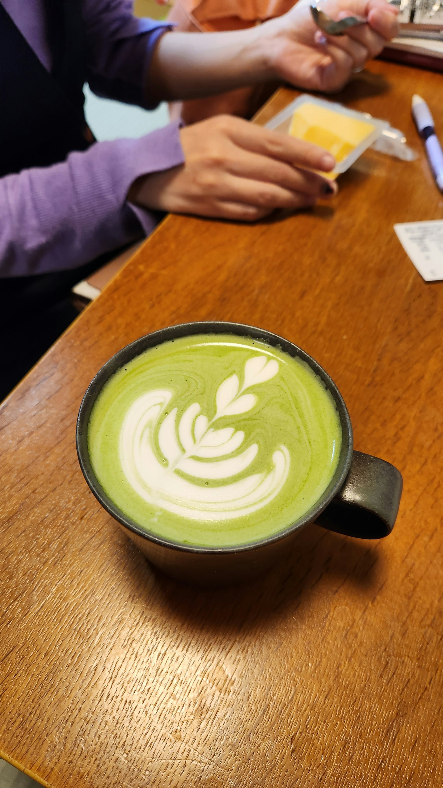 木桌上的抹茶拿铁杯和一只手