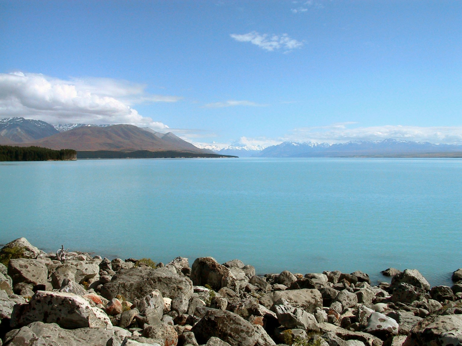Vista escénica de un lago azul con montañas al fondo orilla rocosa