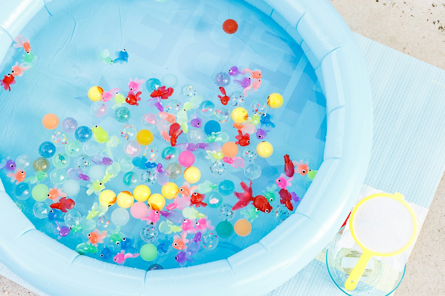 Bola berwarna-warni dan ikan mas merah mengapung di kolam biru
