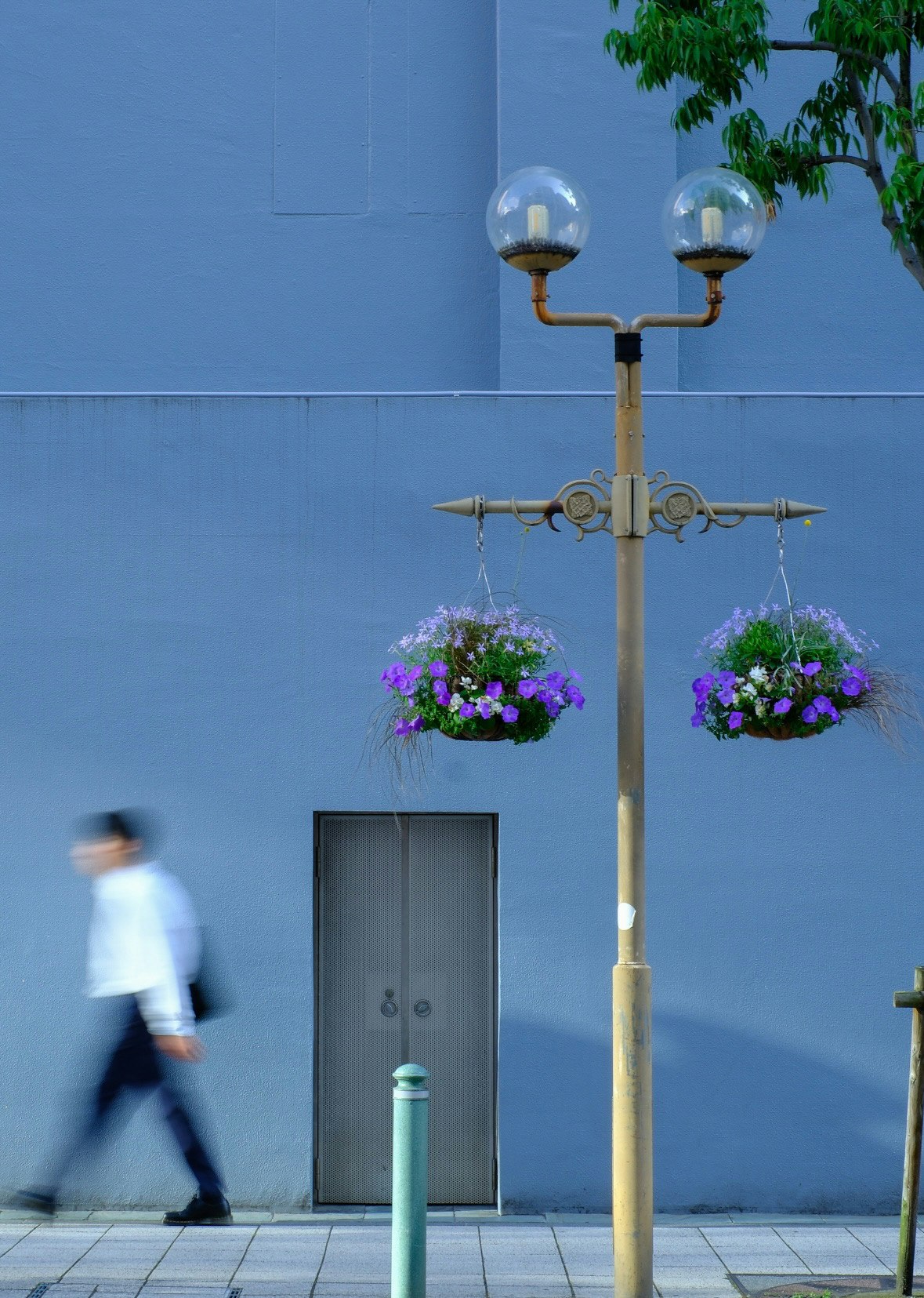 Straßenlaterne mit Blumenkästen vor einer blauen Wand