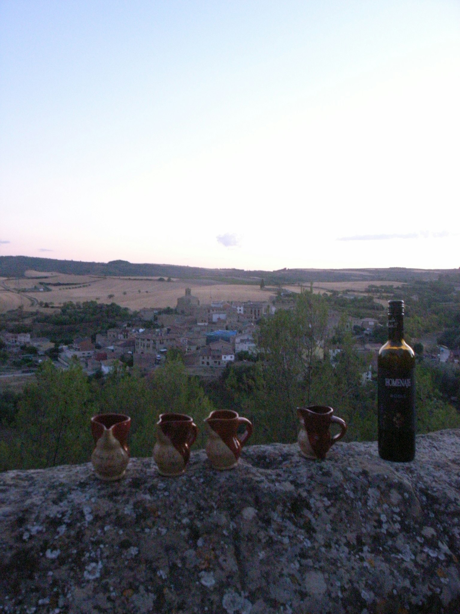 A scenic view with a wine bottle and ceramic cups against a sunset sky