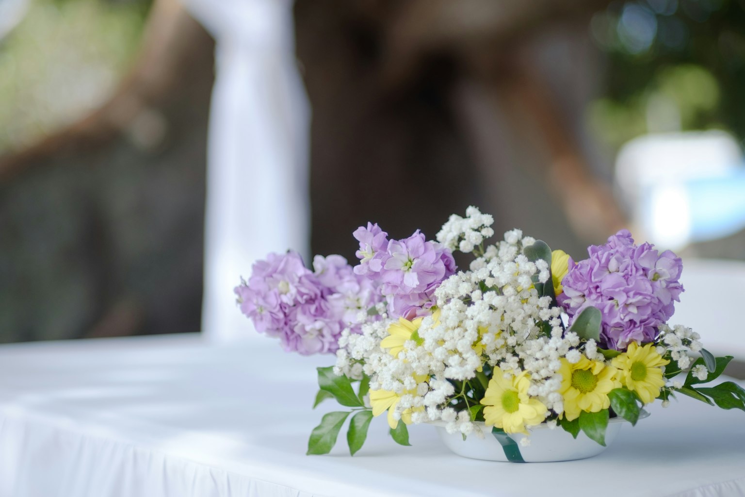 Blumenarrangement mit lila und gelben Blumen auf einem weißen Tischdecken