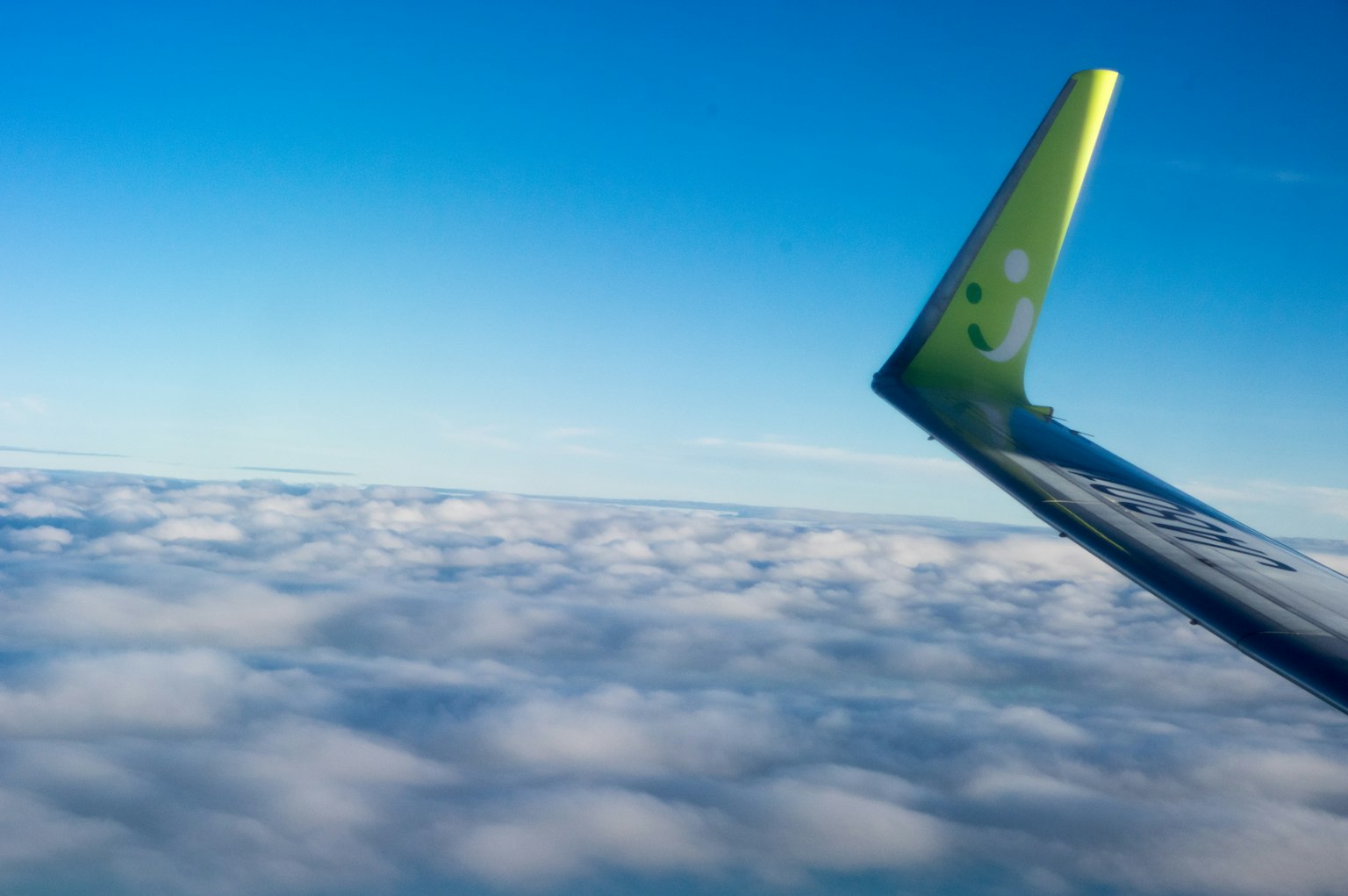 Estremità dell'ala di un aereo sopra nuvole soffici sotto un cielo blu chiaro