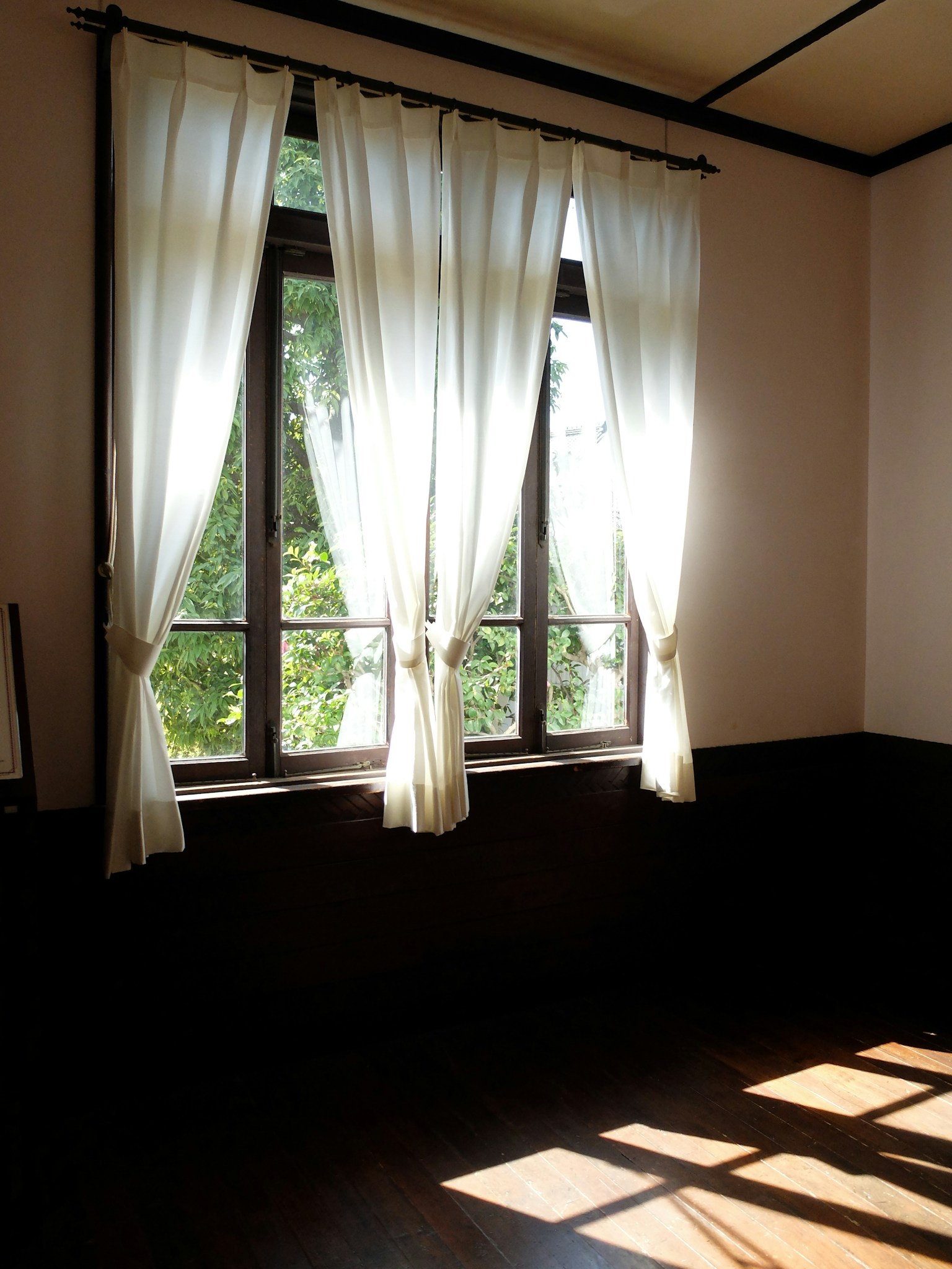Room with sunlight streaming through a window and white curtains
