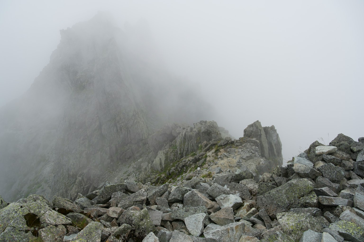 Nebliger Berggipfel mit steinigem Vordergrund