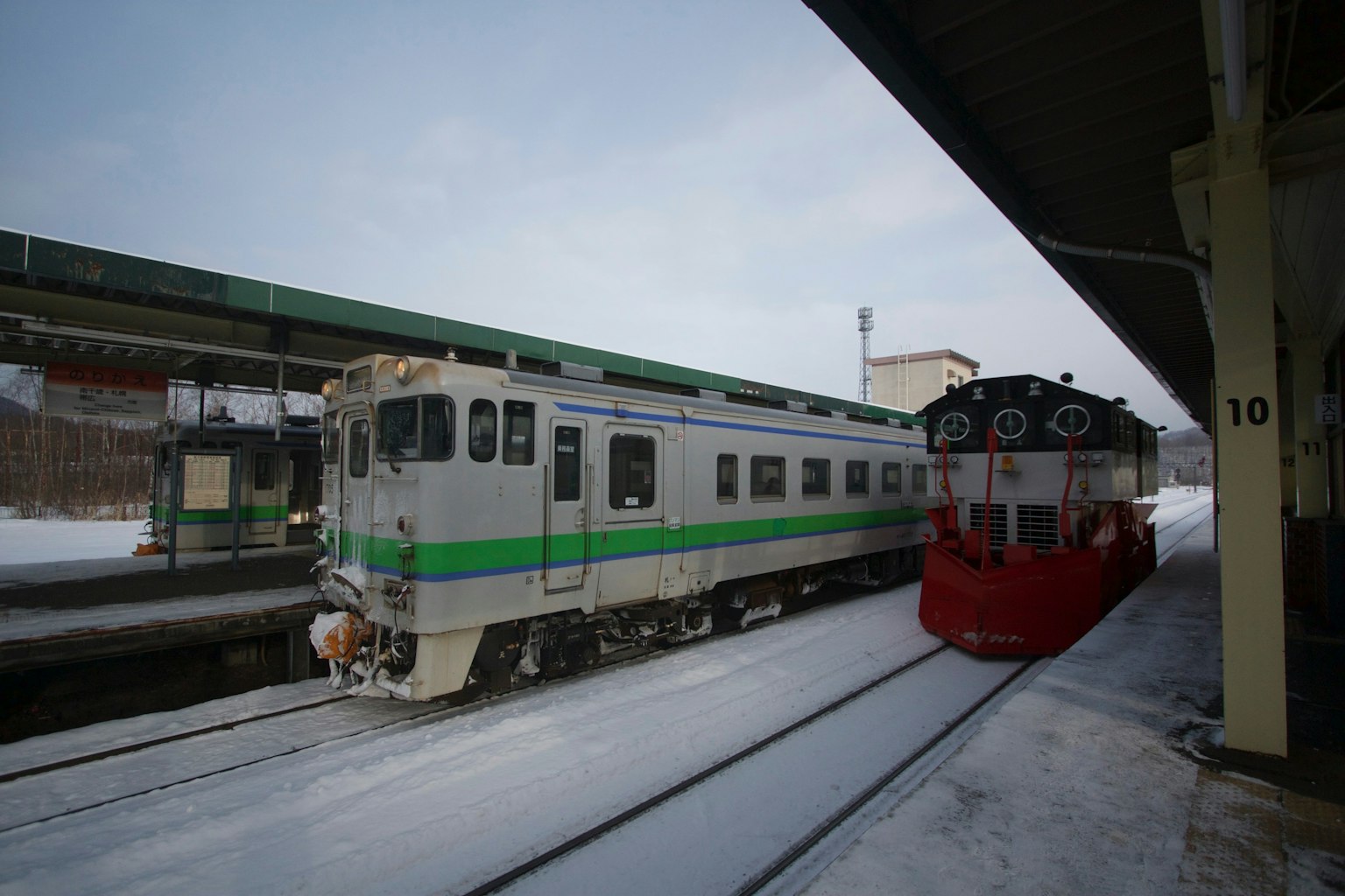 รถไฟสีเขียวและขาวกับหัวรถจักรสีแดงที่สถานีที่มีหิมะตก