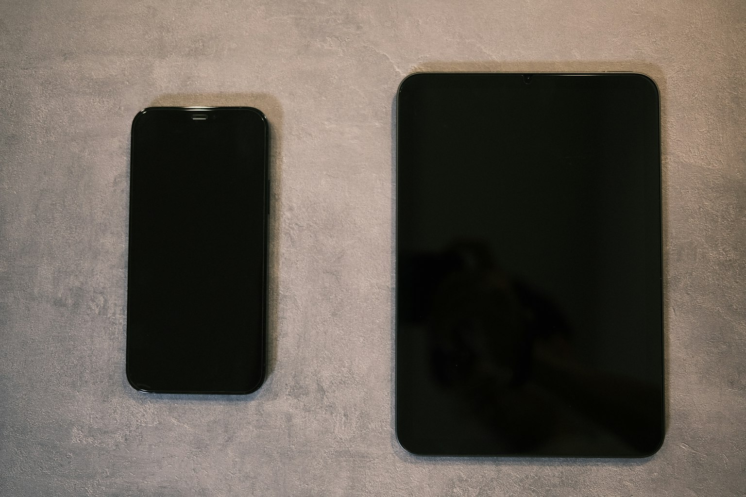 Ein Smartphone und ein Tablet nebeneinander auf einer grauen Oberfläche