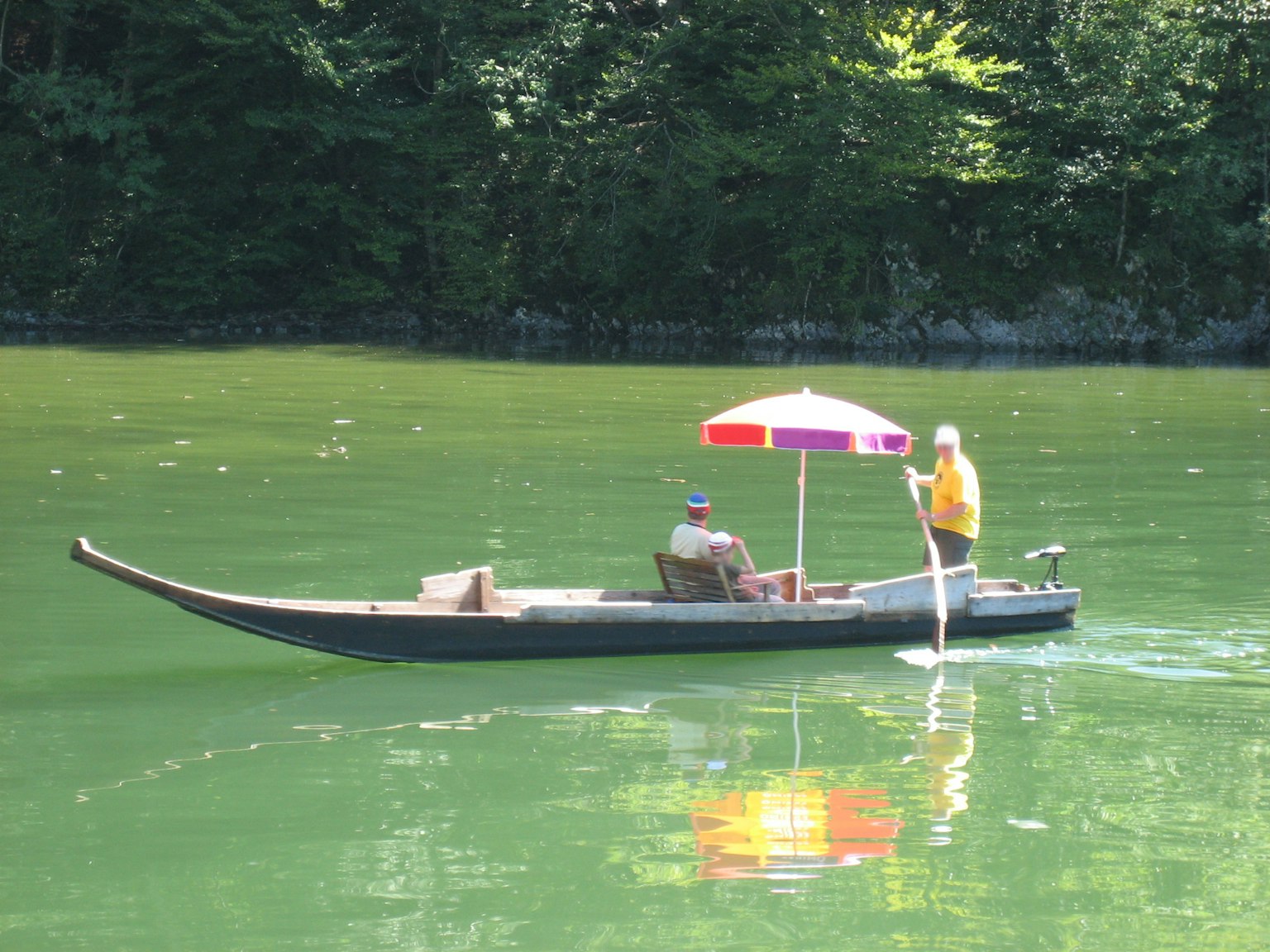 เรือในน้ำสีเขียวกับคนพายที่ถือร่มสีสันสดใส