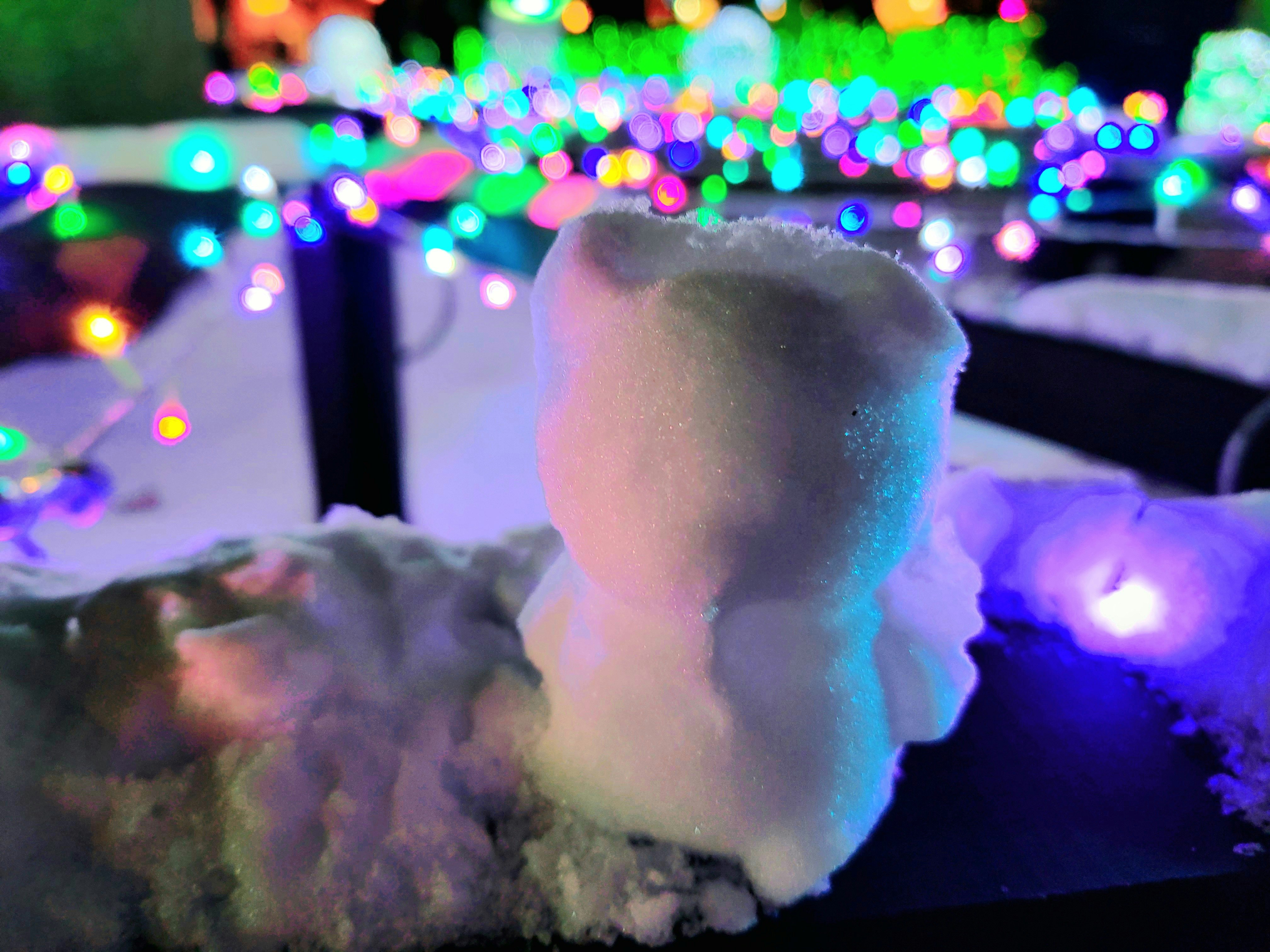 雪だるまとイルミネーションの光がにじむ夜の街並み