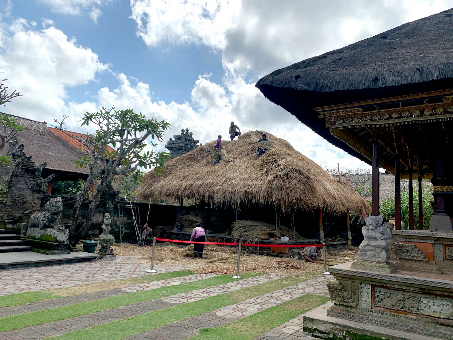Rumah tradisional Bali dengan atap jerami dan pura dalam pemandangan yang indah
