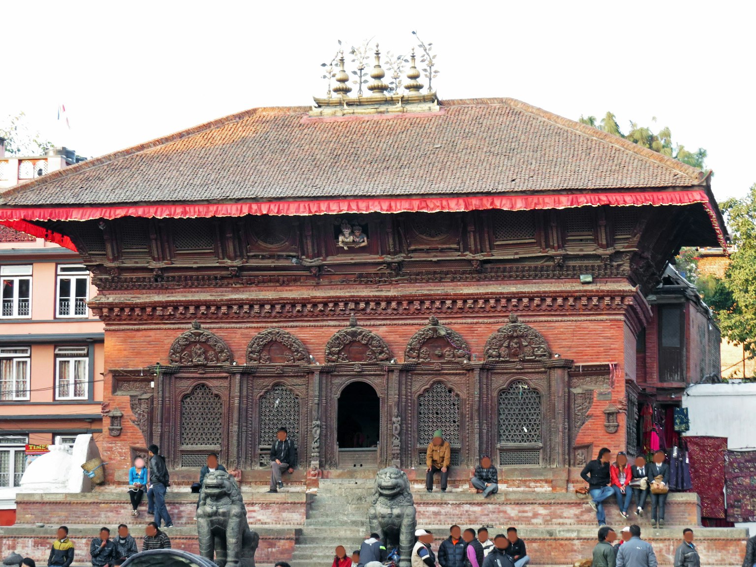 Sebuah kuil tradisional Nepal dengan ukiran rumit dan atap merah dengan orang-orang berkumpul di sekitarnya